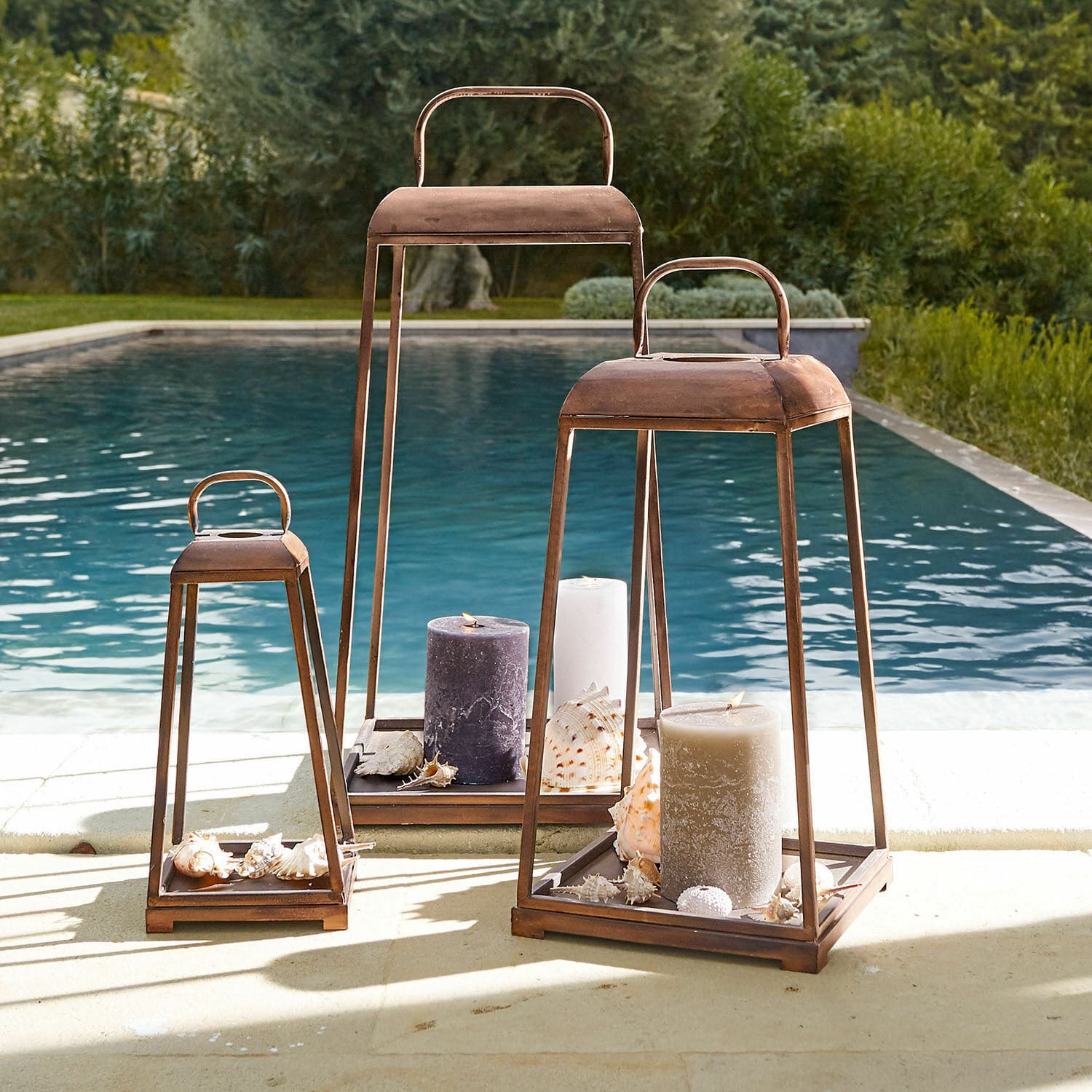 Set di 3 lanterne Martie Tre lanterne in metallo arrugginito con grandi candele e conchiglie vicino alla piscina