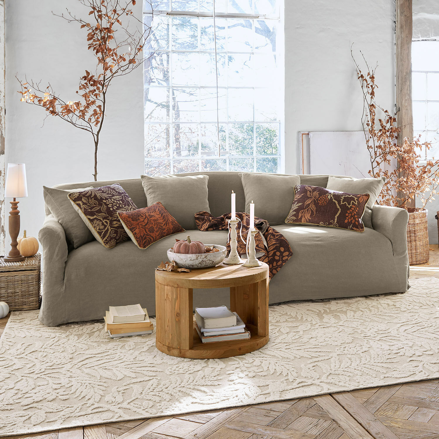Divano Riveneuve Divano beige in tessuto in soggiorno luminoso con tavolino rotondo in legno e decorazioni autunnali