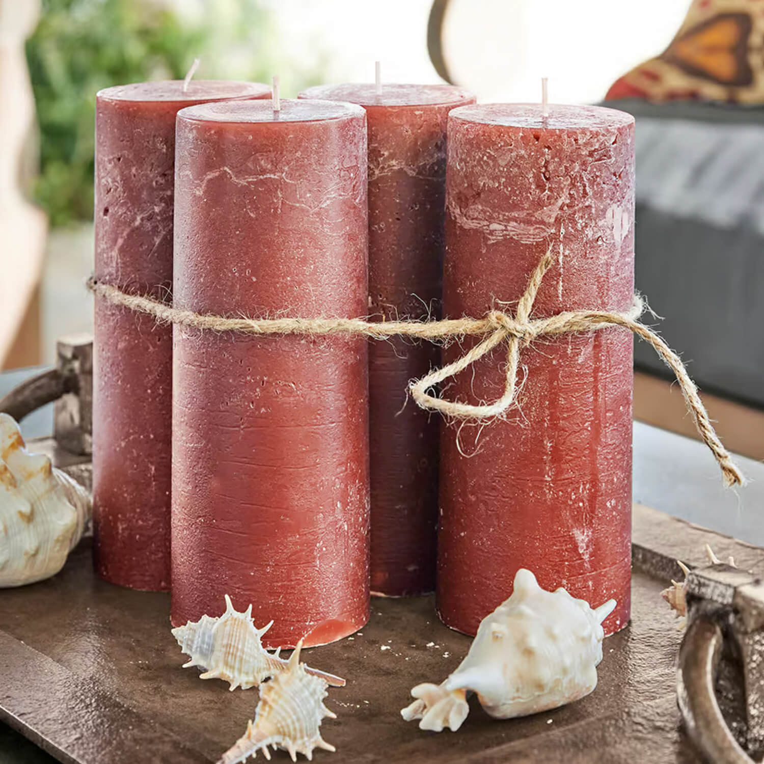 Quattro candele rosse in cera legate con corda naturale su vassoio decorativo con conchiglie