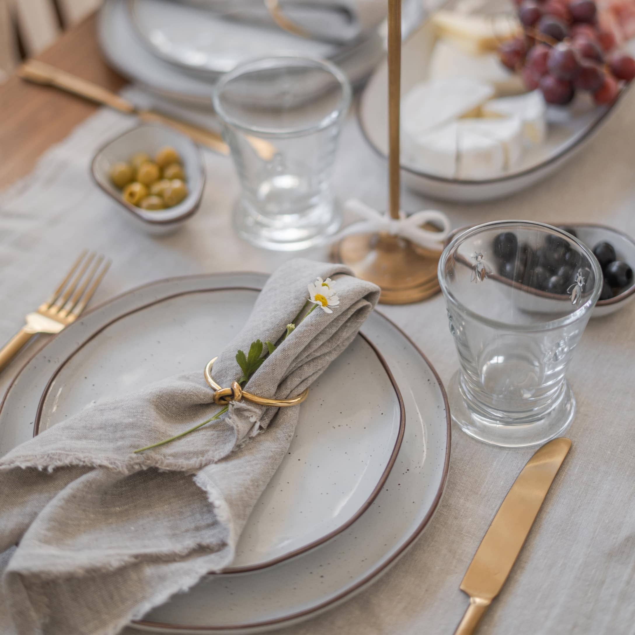 Elegante servizio da tavola con piatti grigi, posate dorate e tovagliolo di lino con fiore