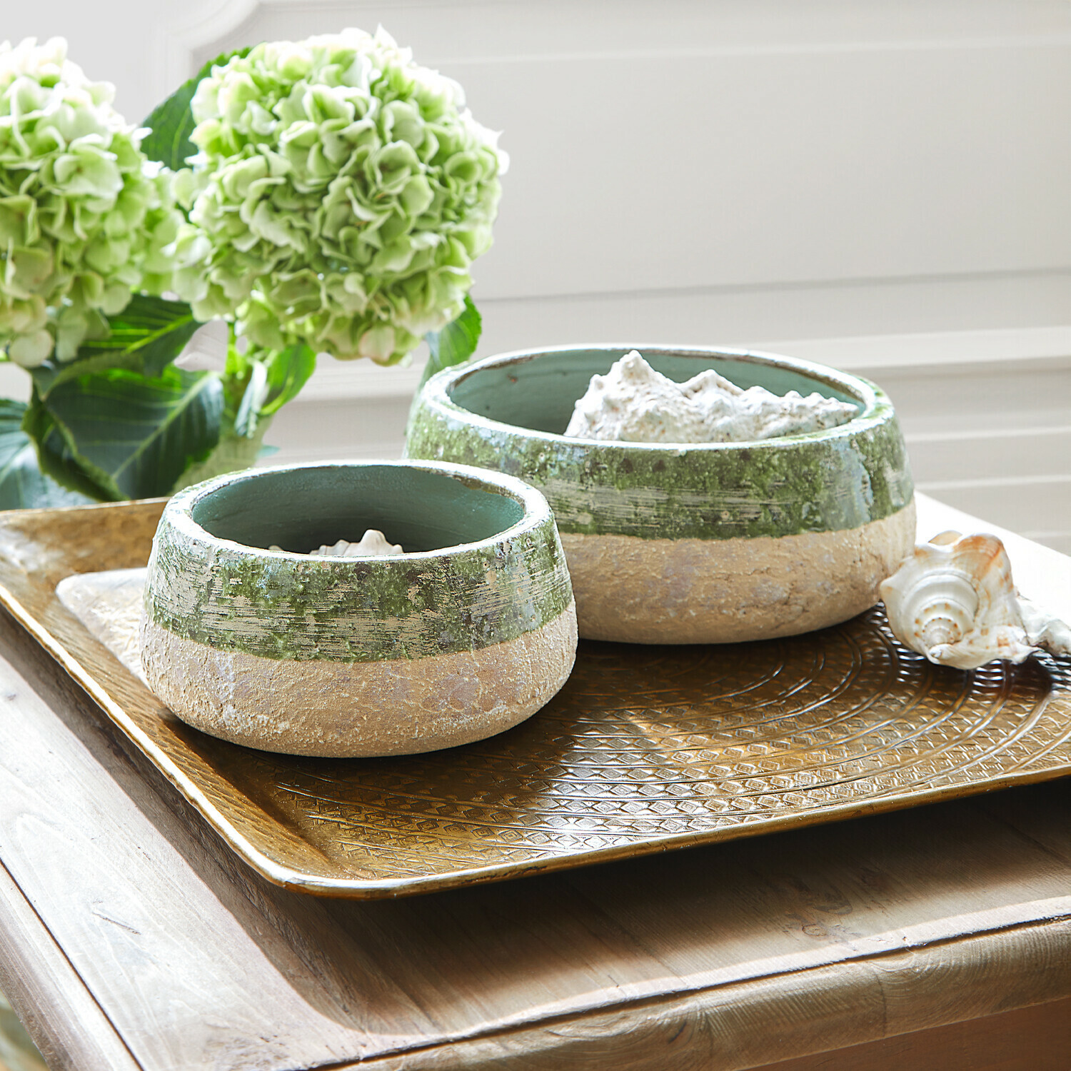 Coppia di ciotole Reefton Due ciotole in ceramica verde e beige su un vassoio dorato decorativo su tavolo in legno