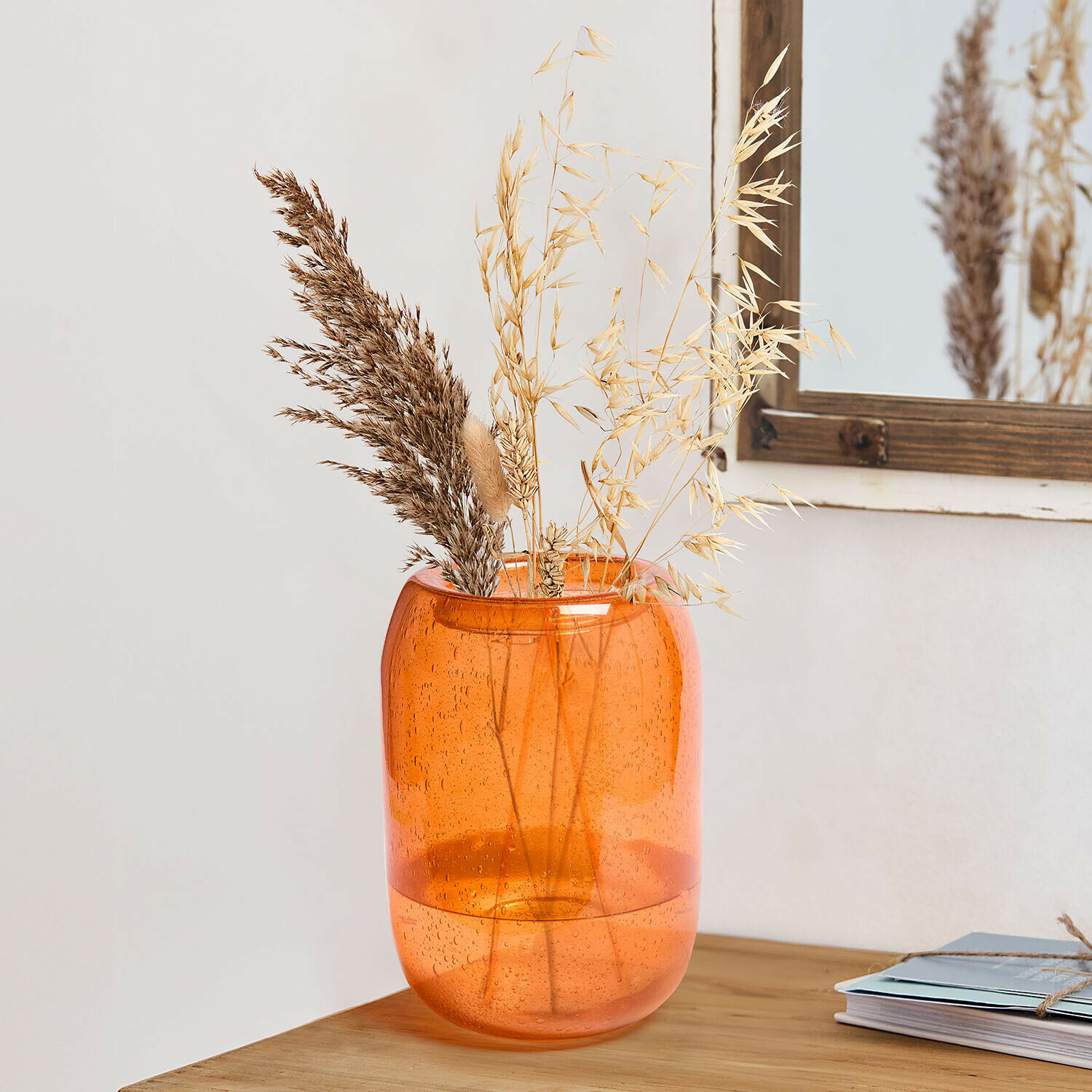 Vaso in vetro arancione con bolle e erbe secche su tavolo in legno, decorazione per interni