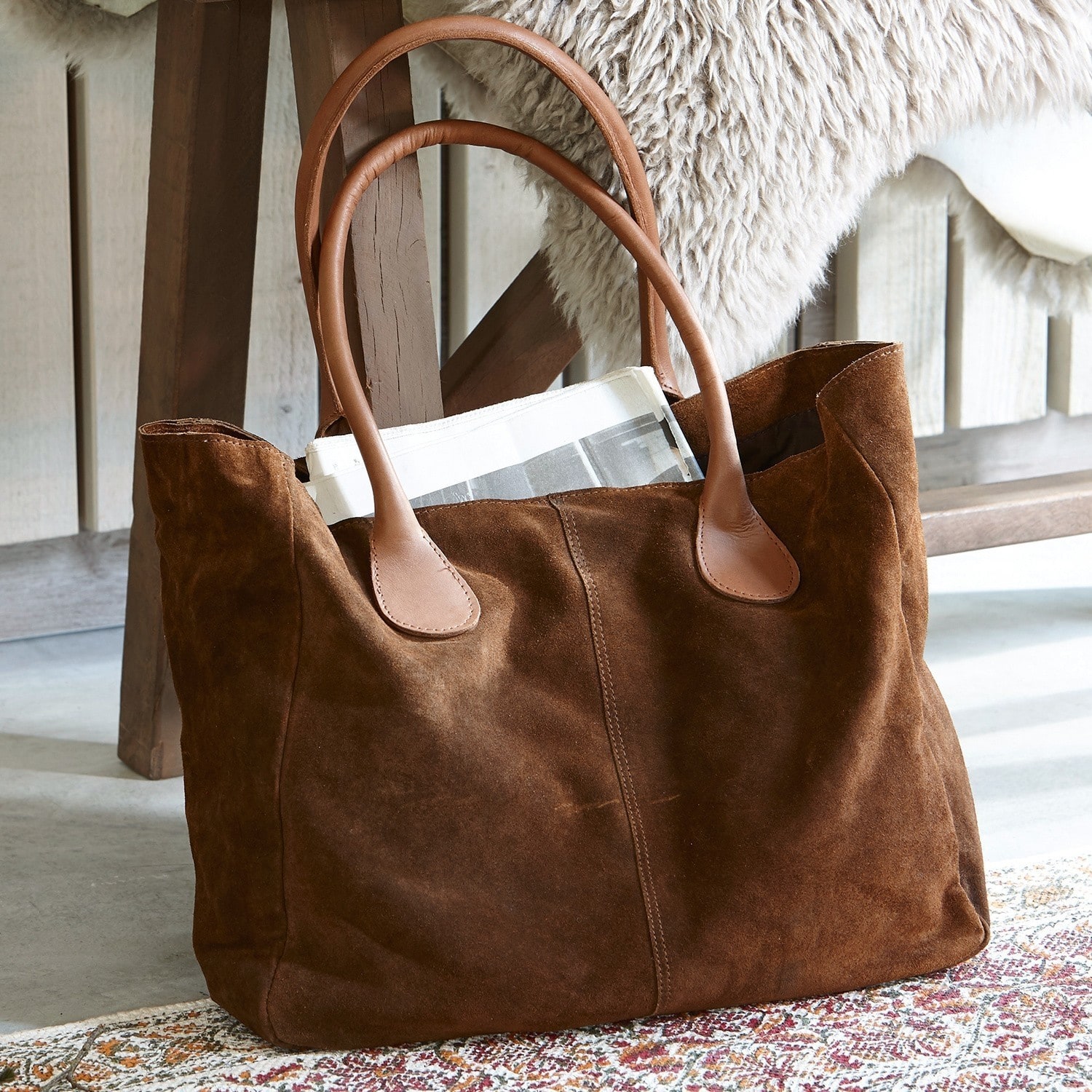 Borsa Genevielle Borsa in camoscio marrone con manici in pelle chiara su tappeto vicino a sedia in legno