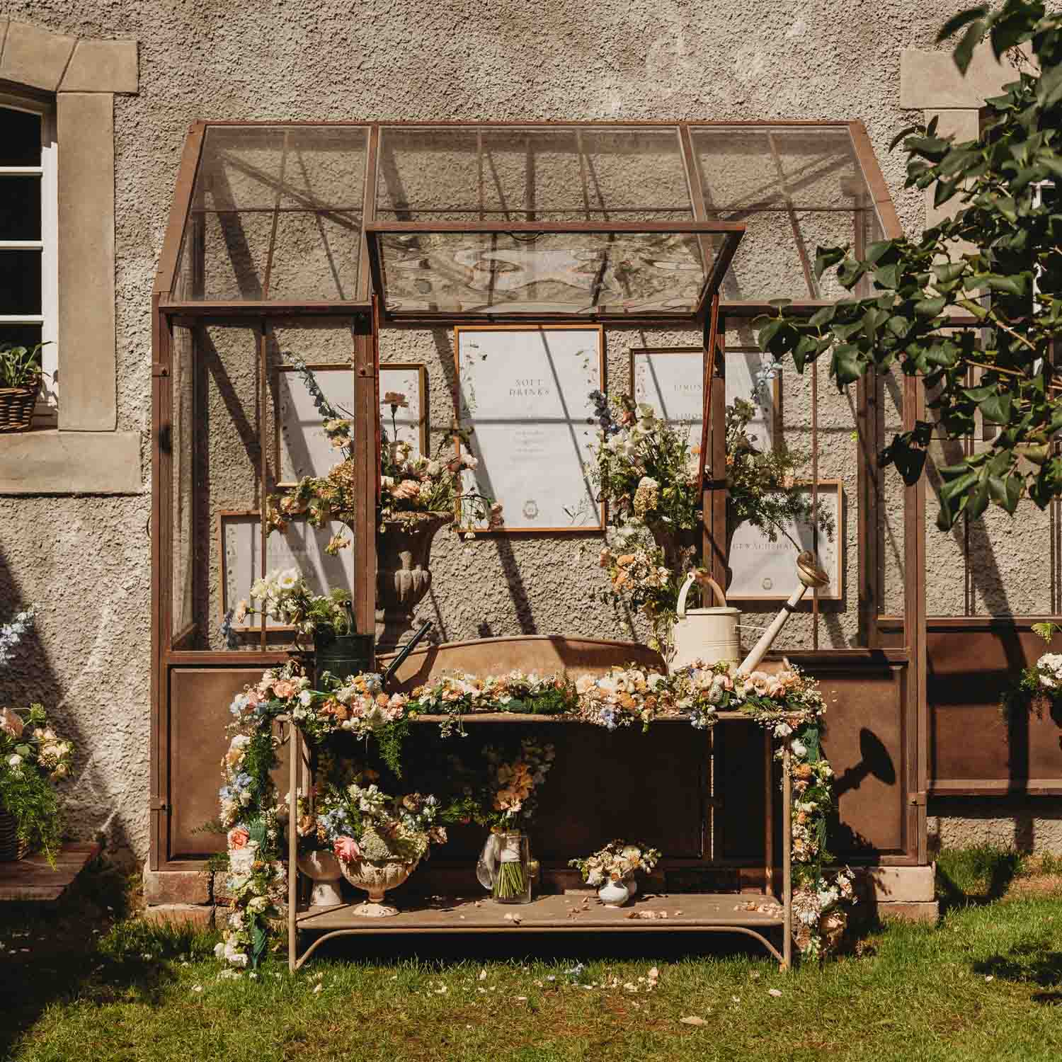 Panca da giardino in metallo rustico decorata con fiori e annaffiatoio davanti a muro con finestra