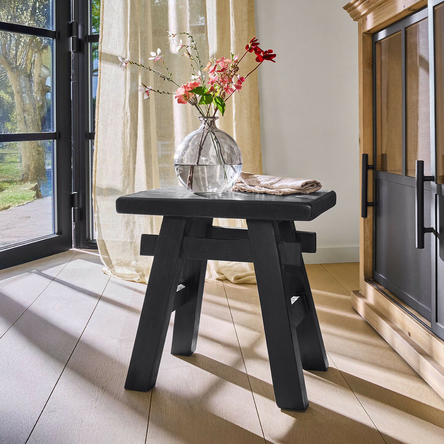 Sgabello in legno nero con struttura semplice in ambiente luminoso con vaso e fiori