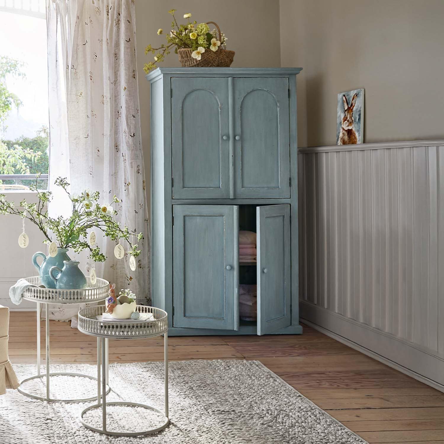 Armadio in legno blu con due ante in interno luminoso con decorazioni floreali e tappeto