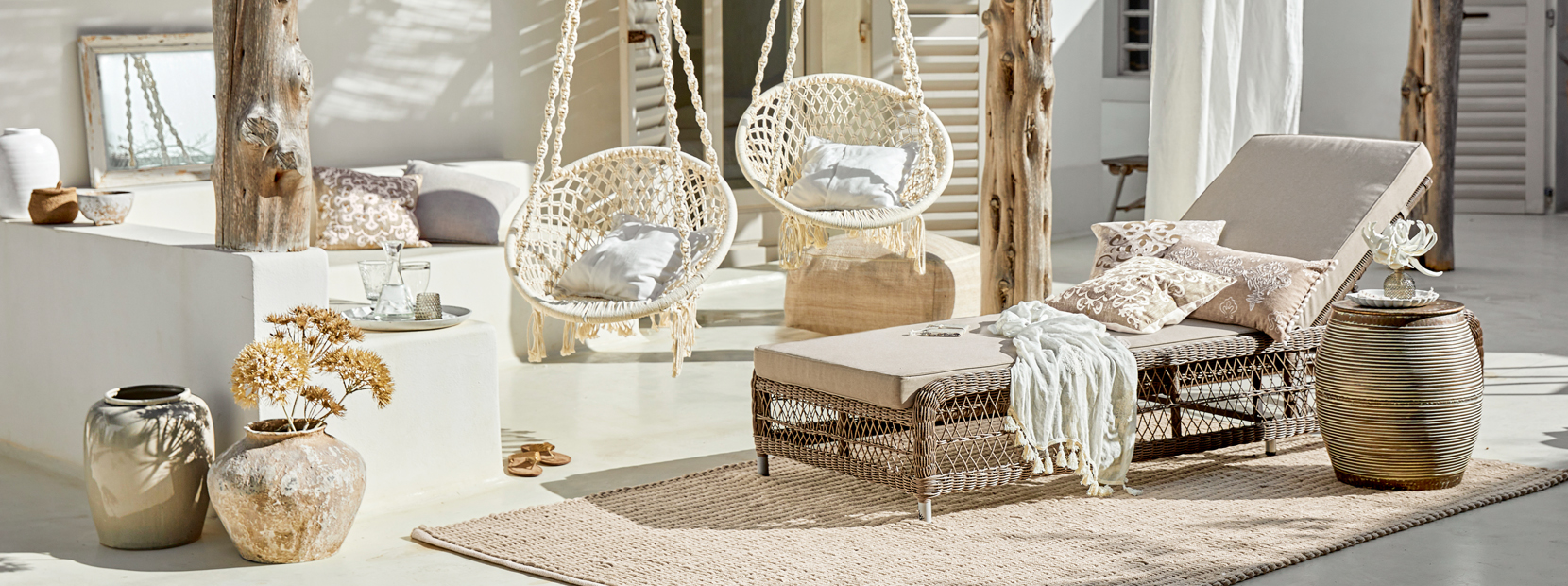 Salotto bohemien con chaise longue in rattan e sedie sospese in cotone dai toni naturali