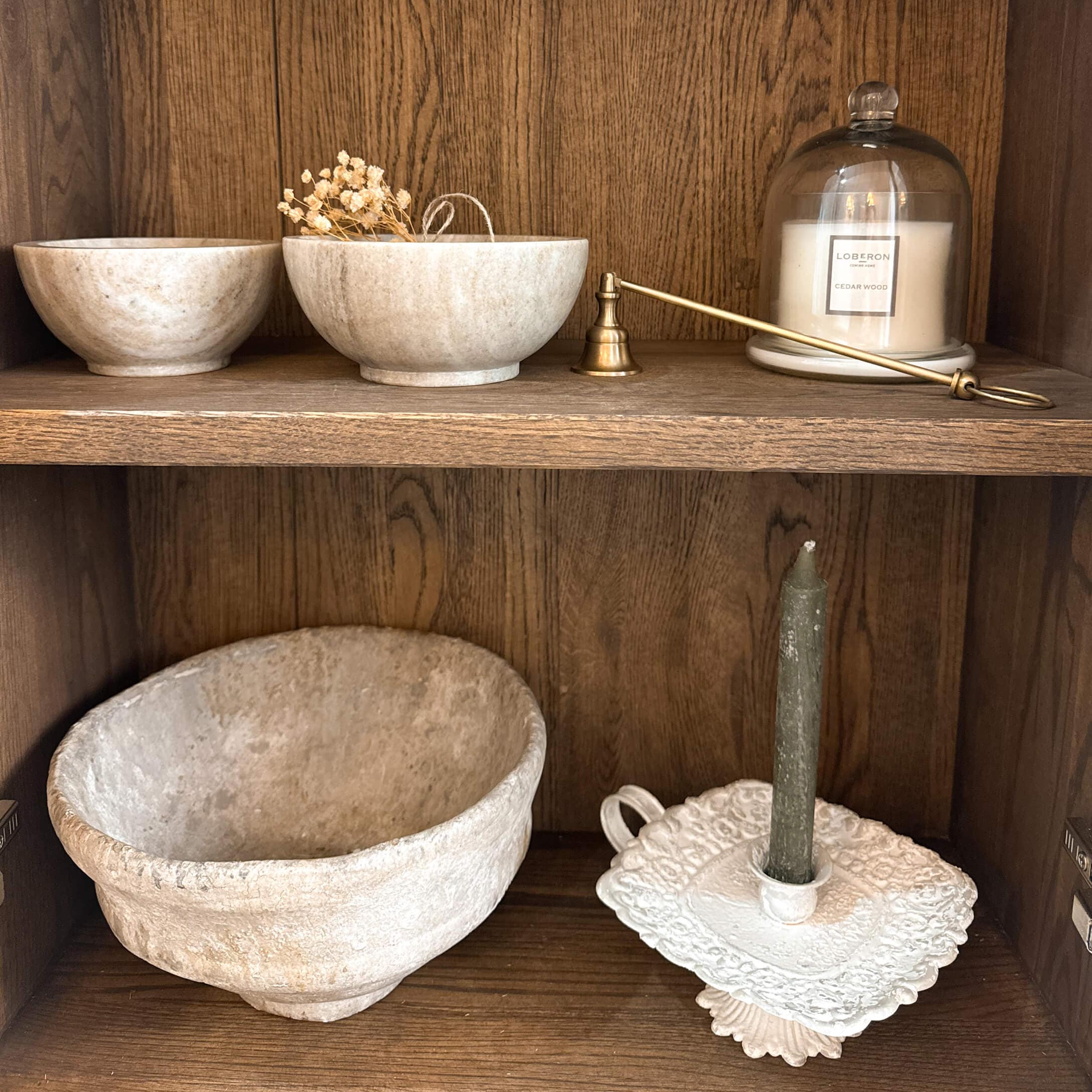 Ciotole decorative in pietra e portacandele con candela verde su mensola in legno rustico
