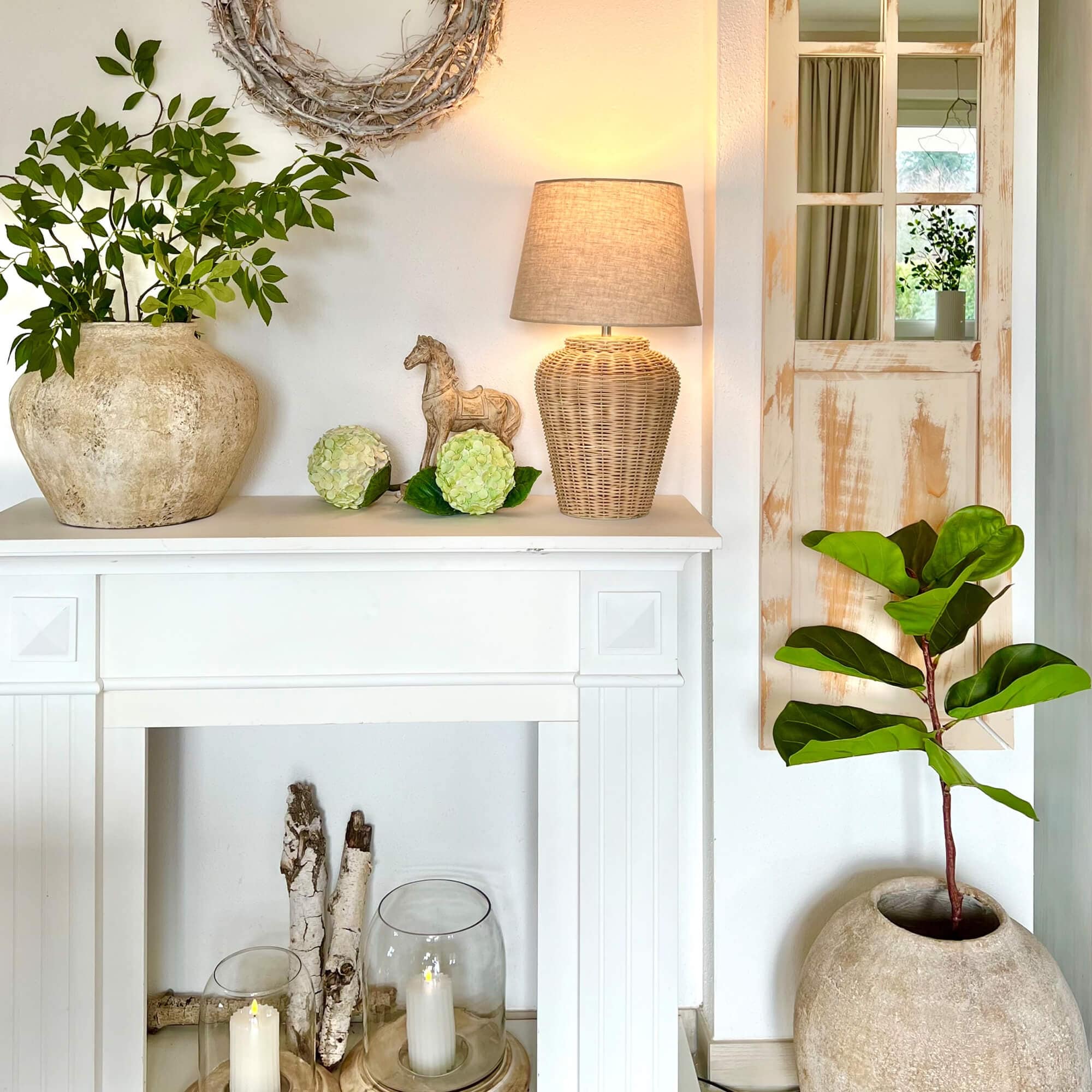 Camino bianco decorativo con lampada in rattan e piante verdi in vasi di pietra