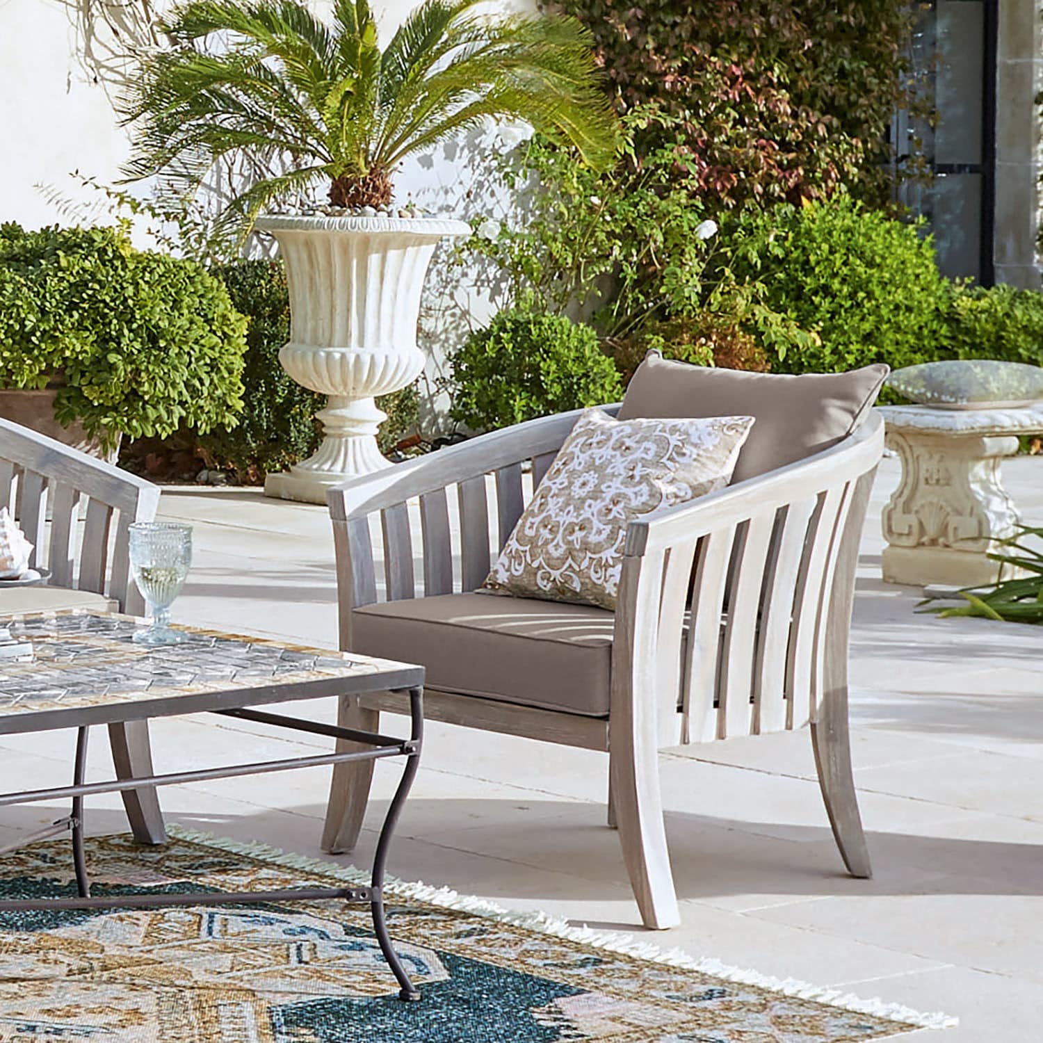 Poltrona Seanad Poltrona da giardino in legno chiaro con cuscini beige su terrazza con piante verdi intorno