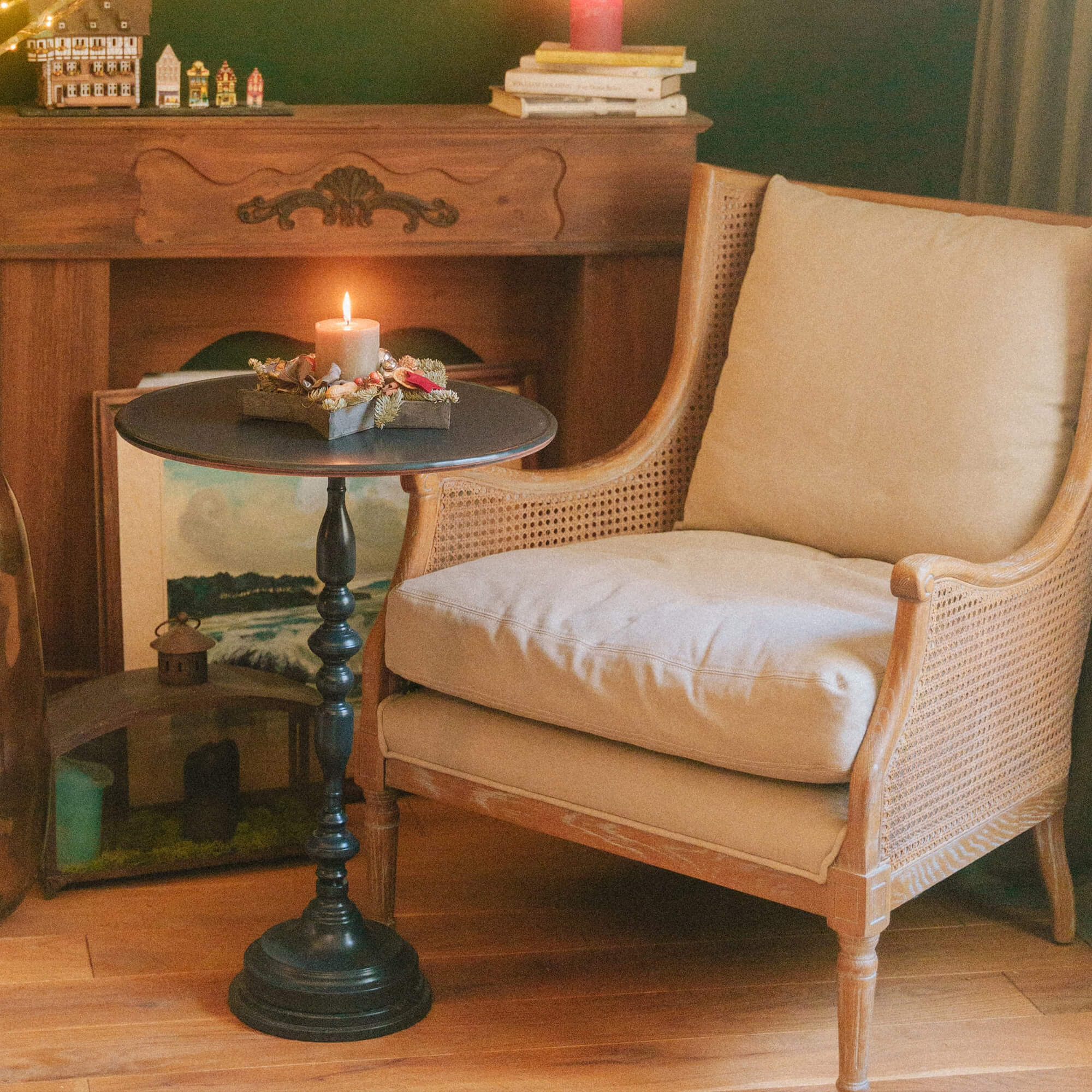 Poltrona in legno con cuscino beige accanto a tavolino nero con candela accesa e decorazioni natalizie