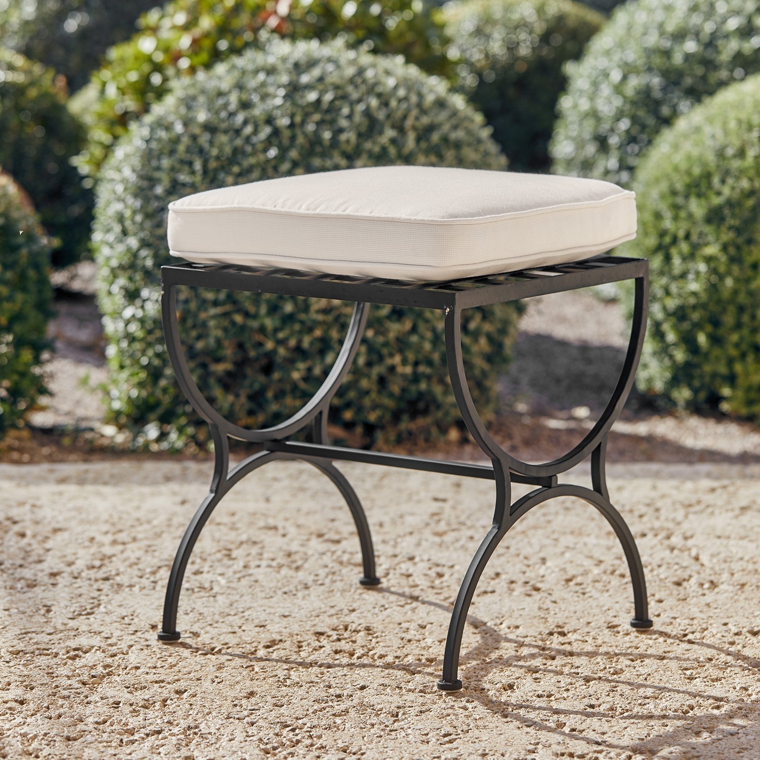 Sgabello Terell Sgabello da giardino in metallo nero con cuscino crema su terreno sabbioso all'aperto