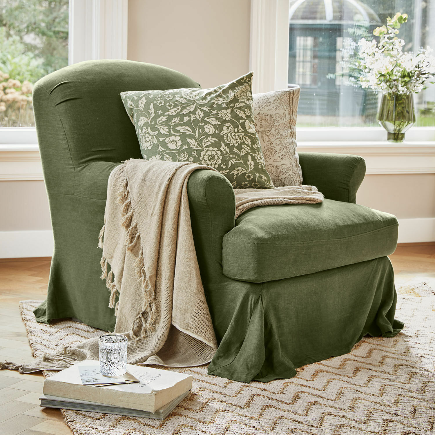 Poltrona Vionnique Poltrona verde in lino con coperta beige e cuscini floreali su tappeto in soggiorno