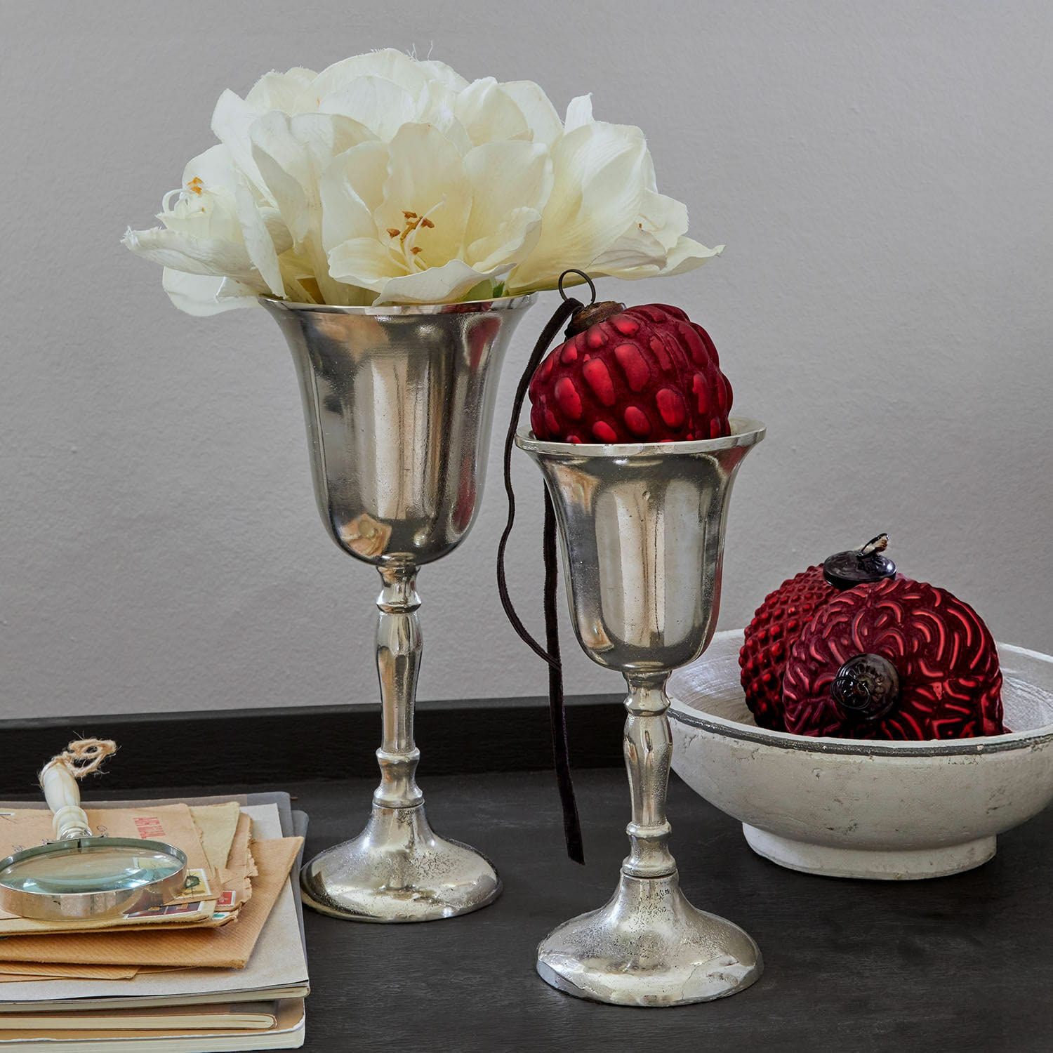 Coppia di vasi Solérie Due coppe decorative argentate con fiori bianchi e ornamenti rossi su tavolo nero