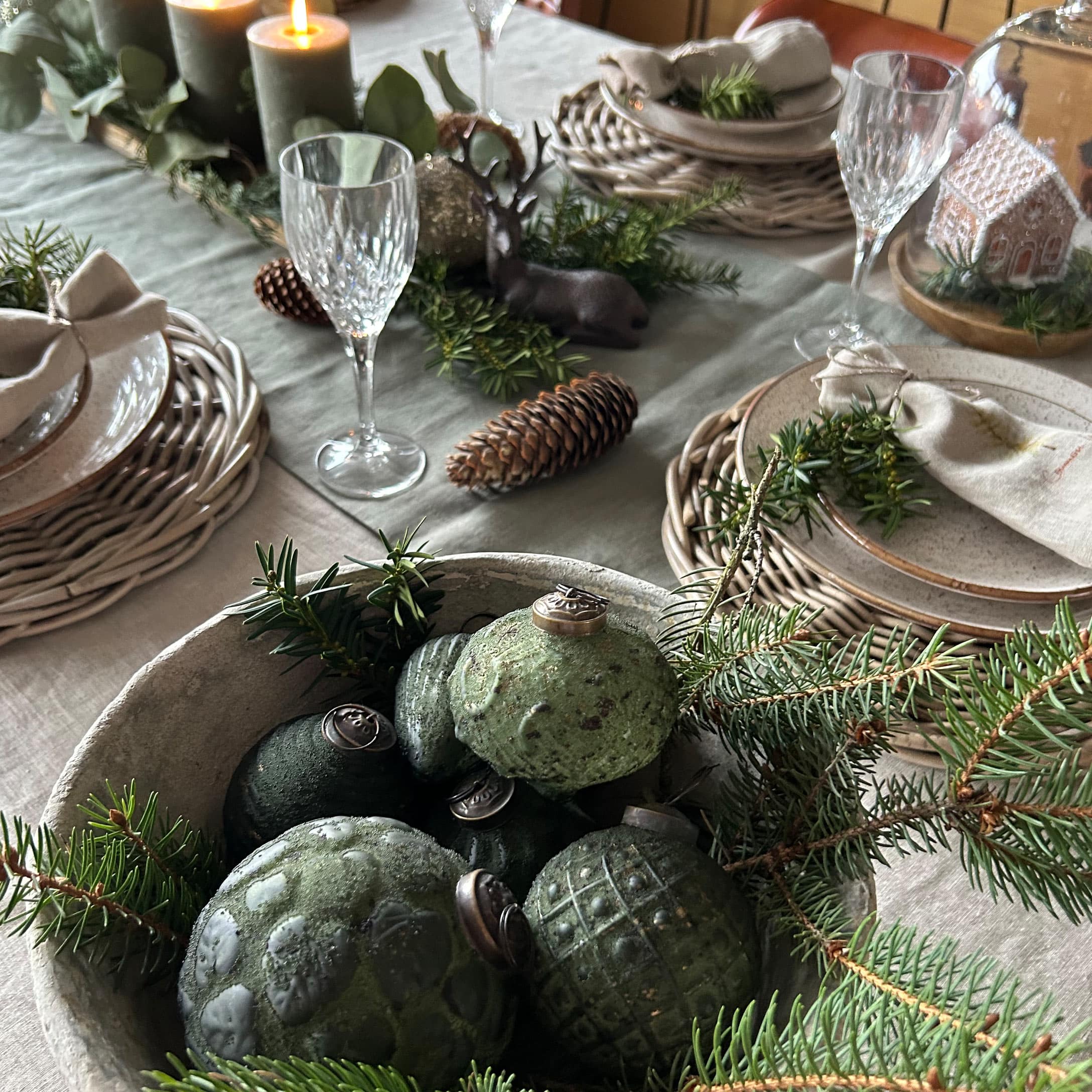 Palle di Natale verdi in ceramica in ciotola con rami di abete su tavola decorata