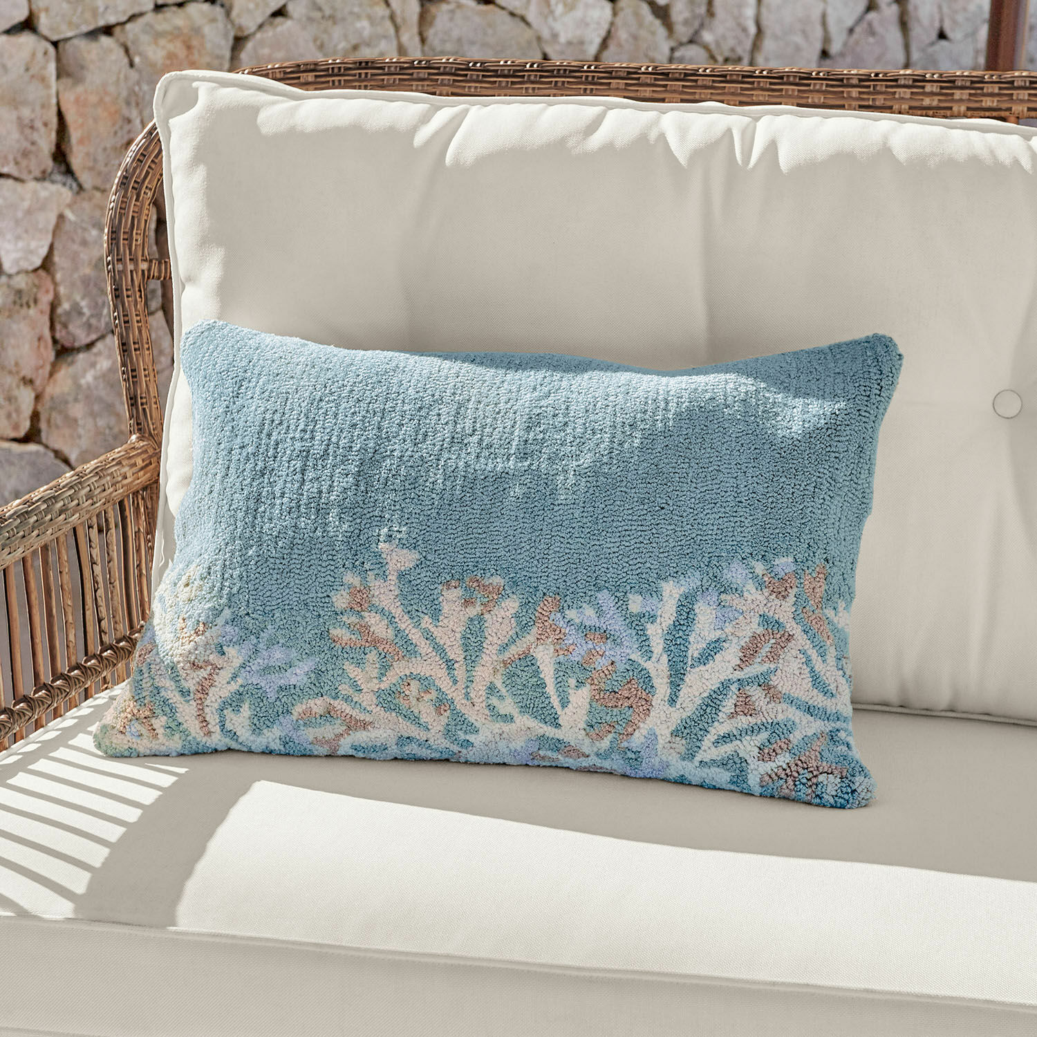 Copricuscino da interni ed esterni Dorlancourt Cuscino decorativo blu in tessuto morbido con motivo corallo su divano chiaro in rattan.
