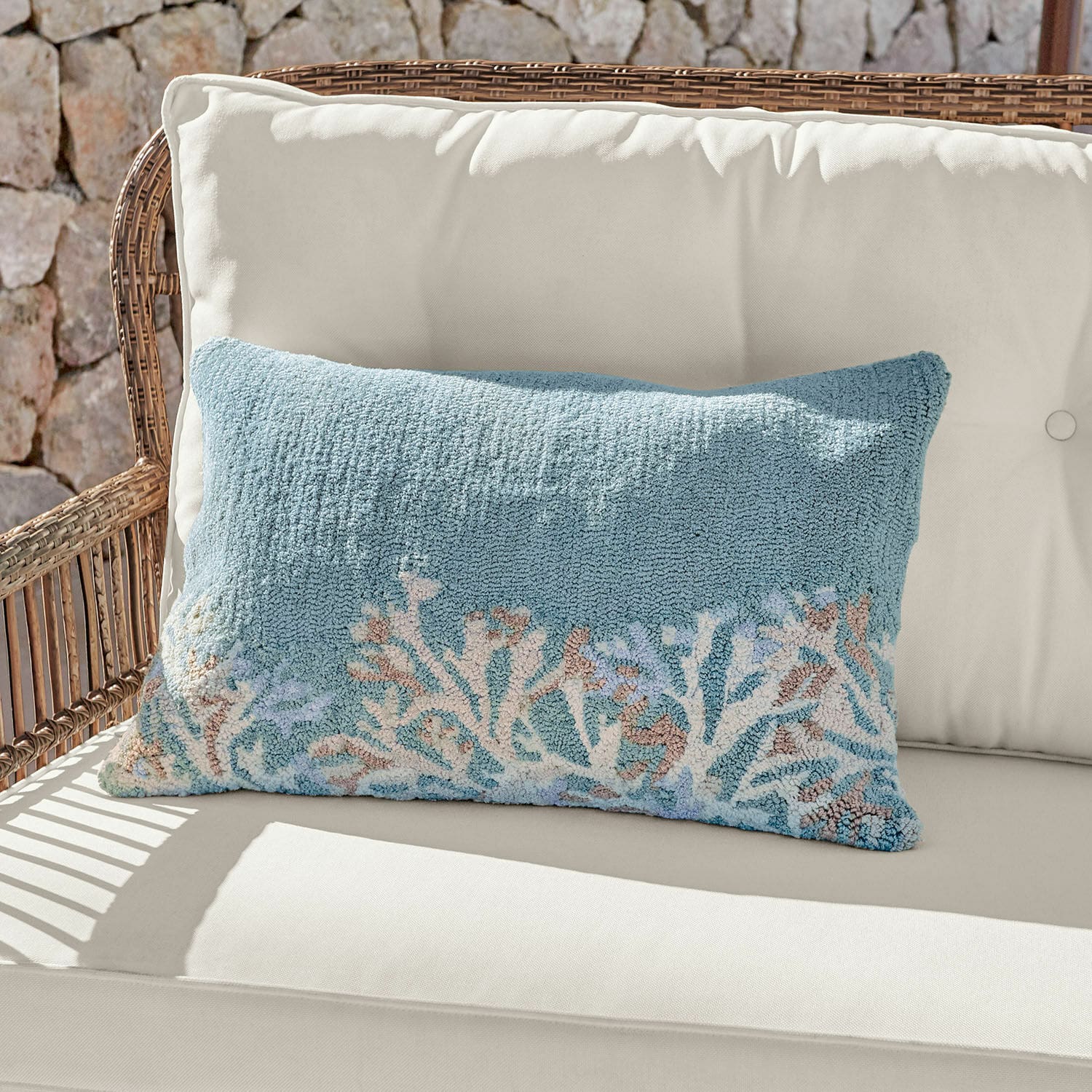 Copricuscino da interni ed esterni Dorlancourt Cuscino decorativo blu in tessuto morbido con motivo corallo su divano chiaro in rattan.