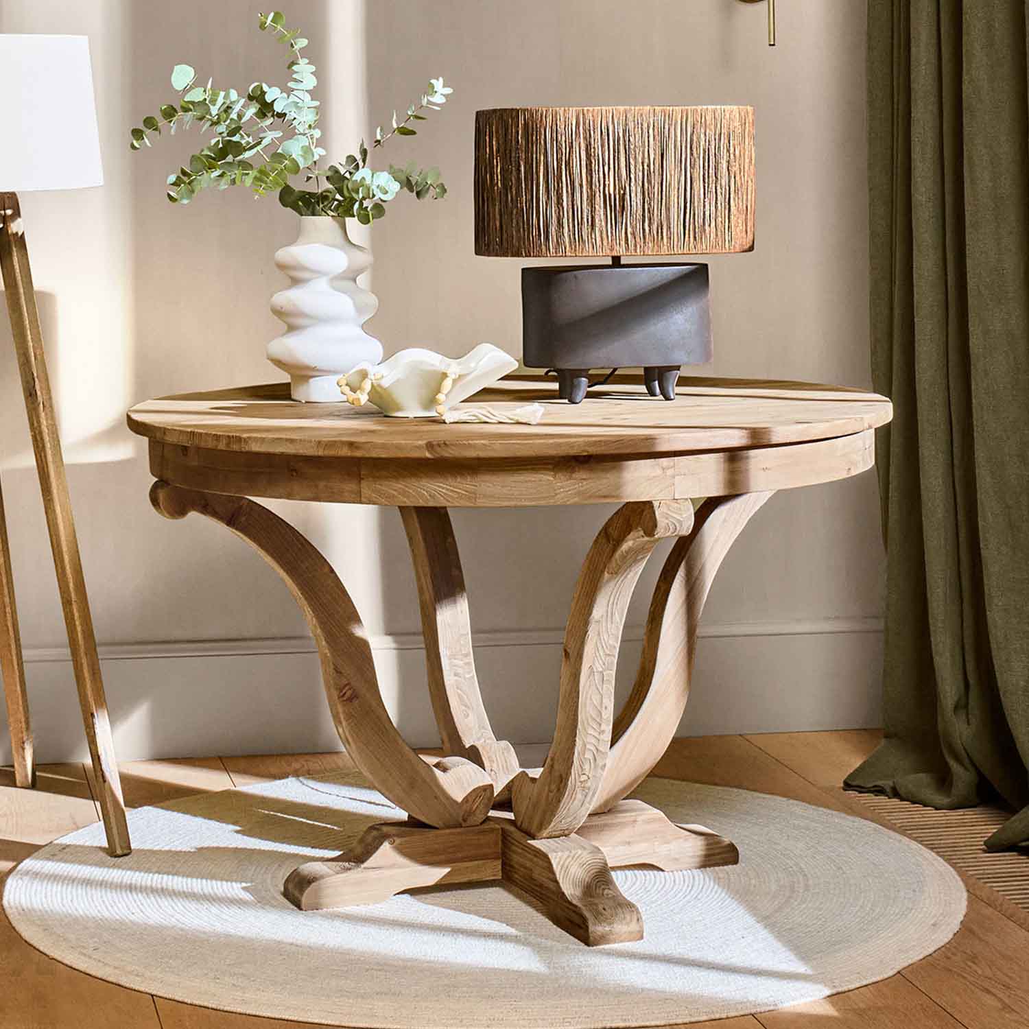 Tavolo rotondo in legno naturale con lampada e vaso decorativo su tappeto chiaro in ambiente accogliente