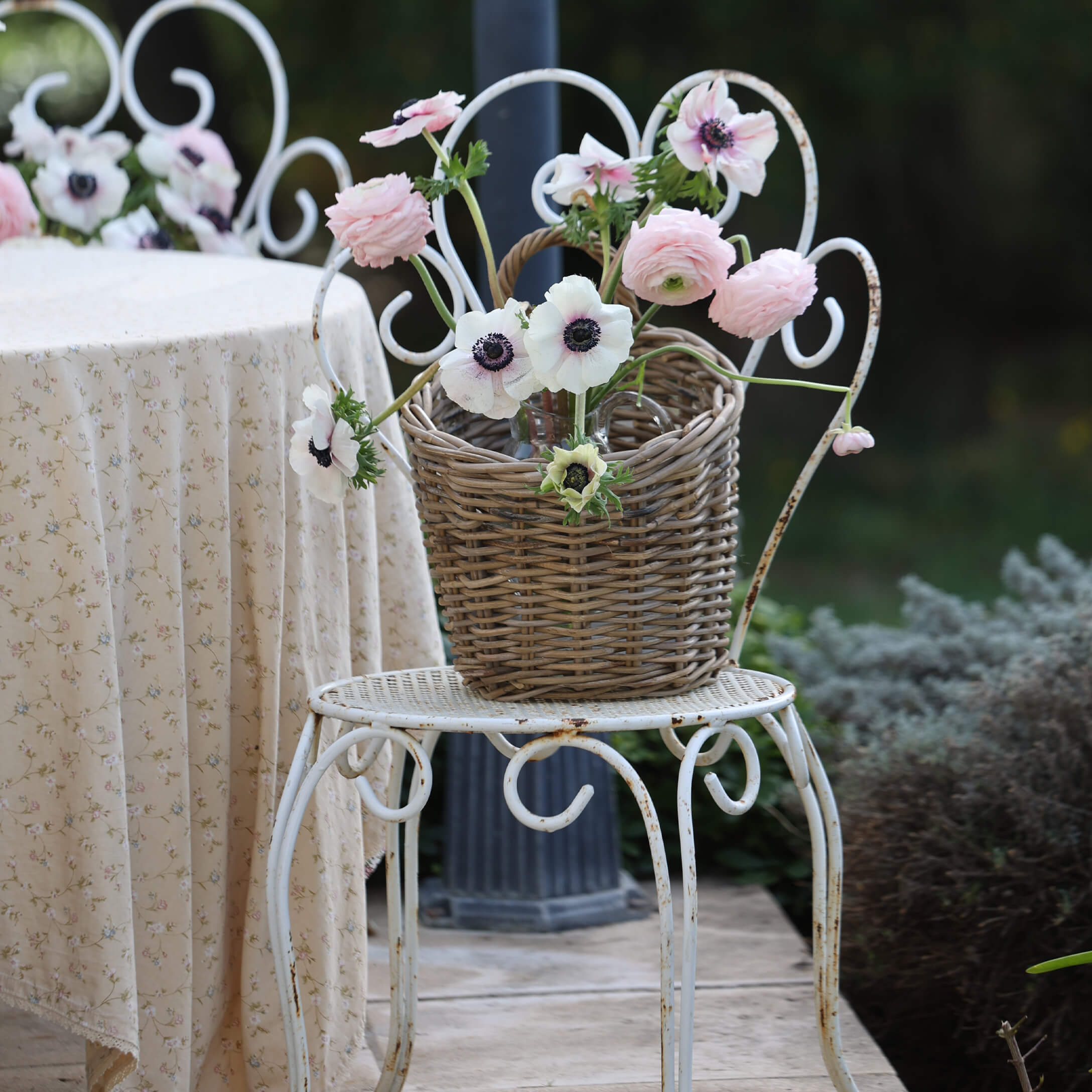 Cesto di vimini con fiori rosa e bianchi su sedia in metallo bianco in giardino
