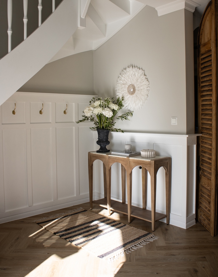 Tappeto naturale beige con righe nere e frange su pavimento in legno chiaro in un ingresso luminoso