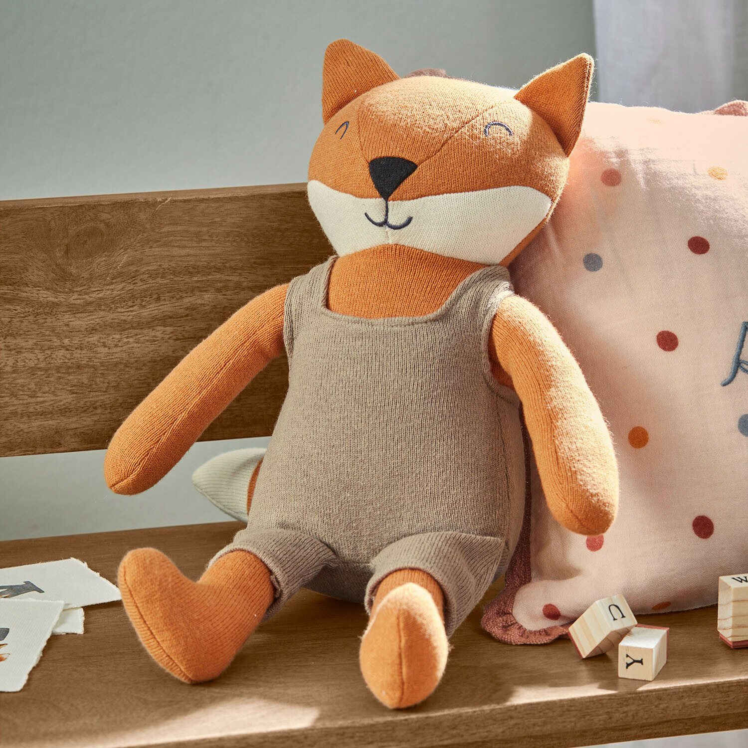 Peluche Fuzzlin Peluche volpe arancione con tuta beige seduta su panca di legno con blocchi di apprendimento