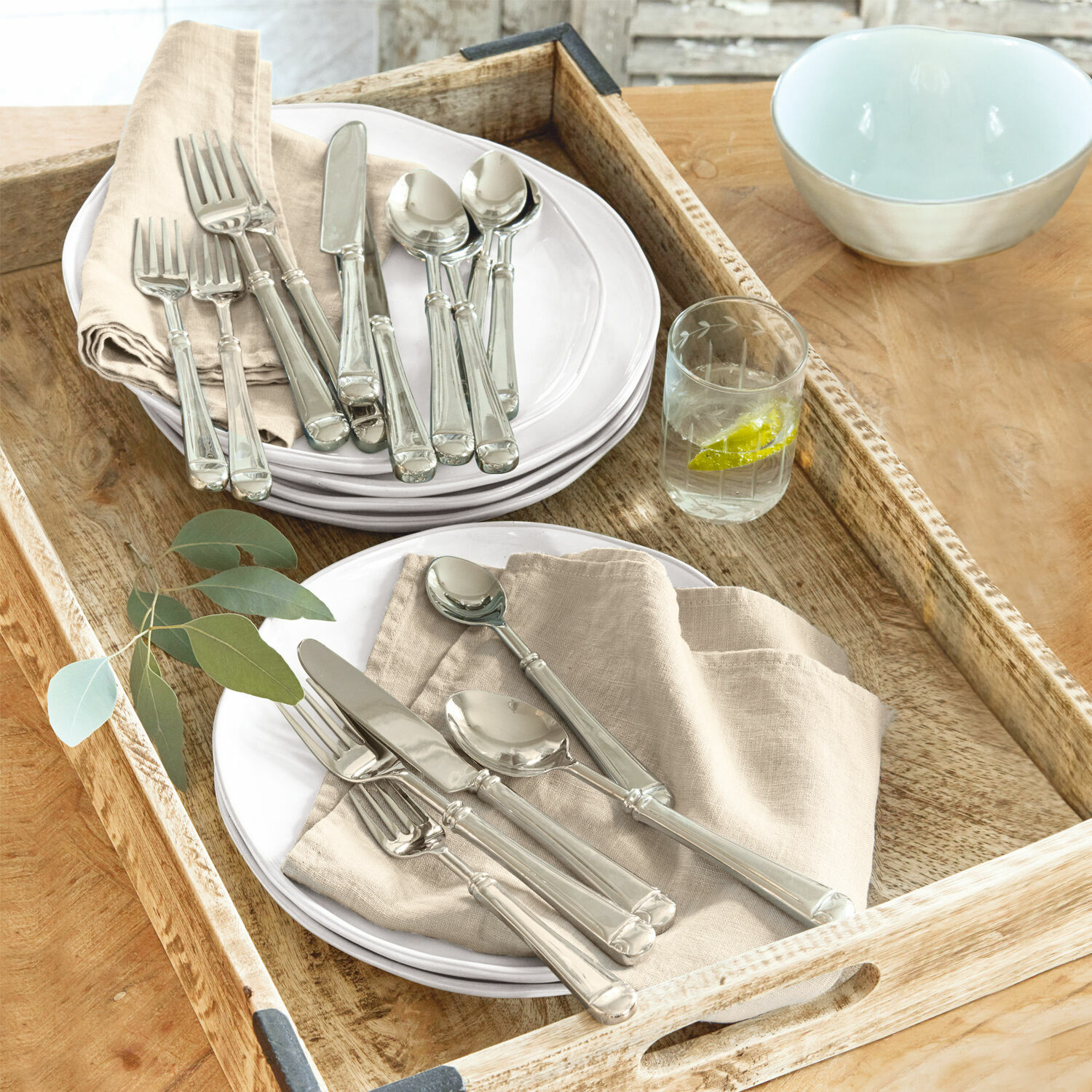 Posate Eriat Set di posate argentate su piatti bianchi con tovaglioli beige su vassoio in legno
