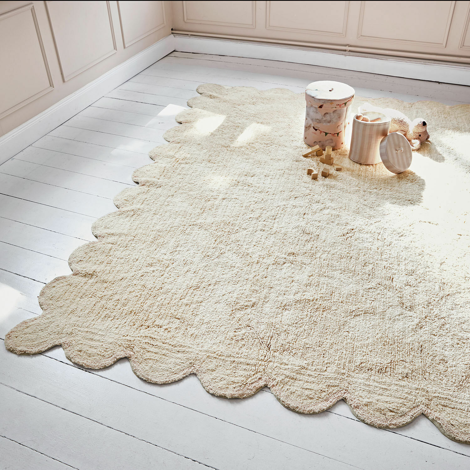 Tappeto Fenvara Tappeto beige in materiale morbido con bordo ondulato su pavimento in legno chiaro in camera bambini