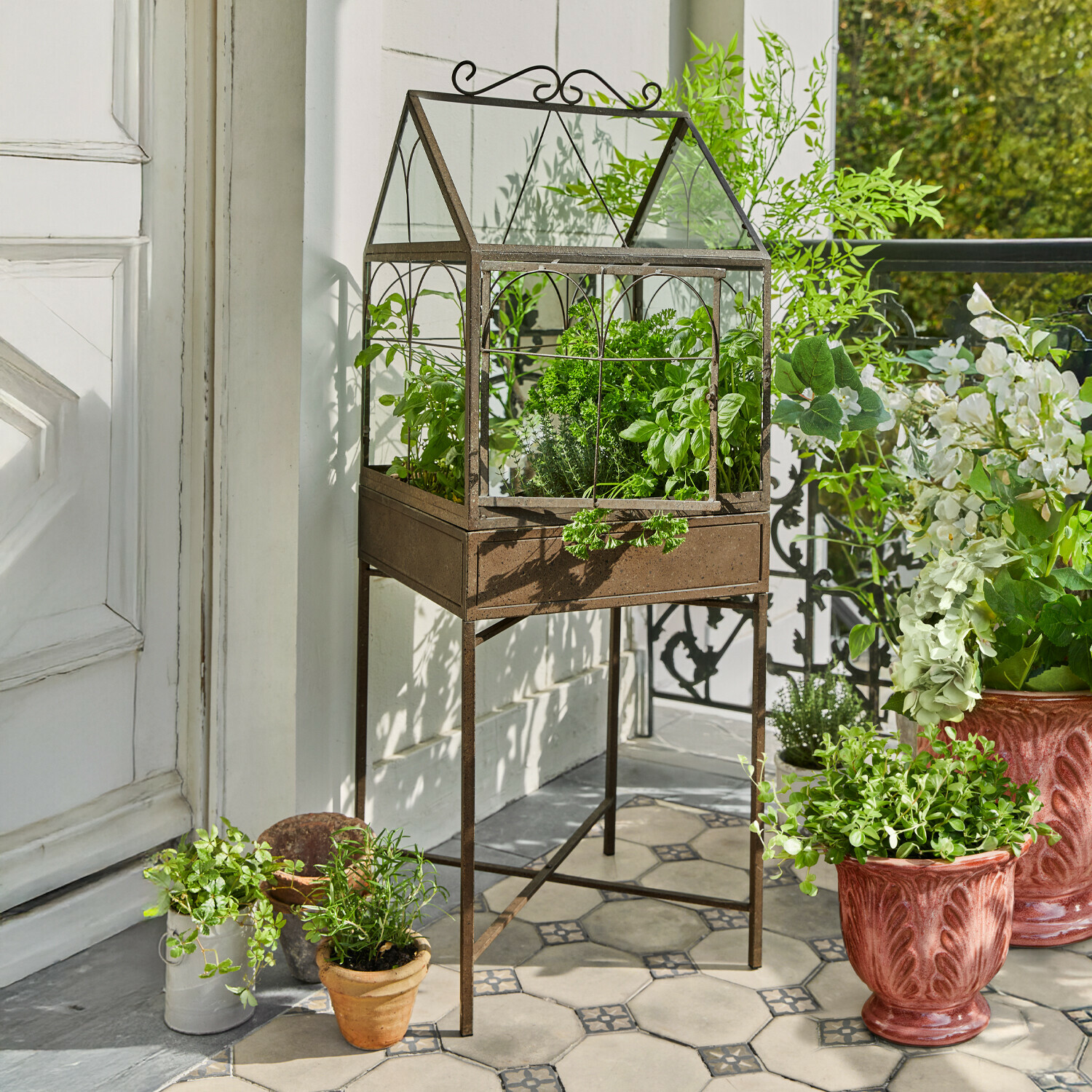 Serra in metallo color ruggine su piedistallo con erbe verdi su terrazza piastrellata