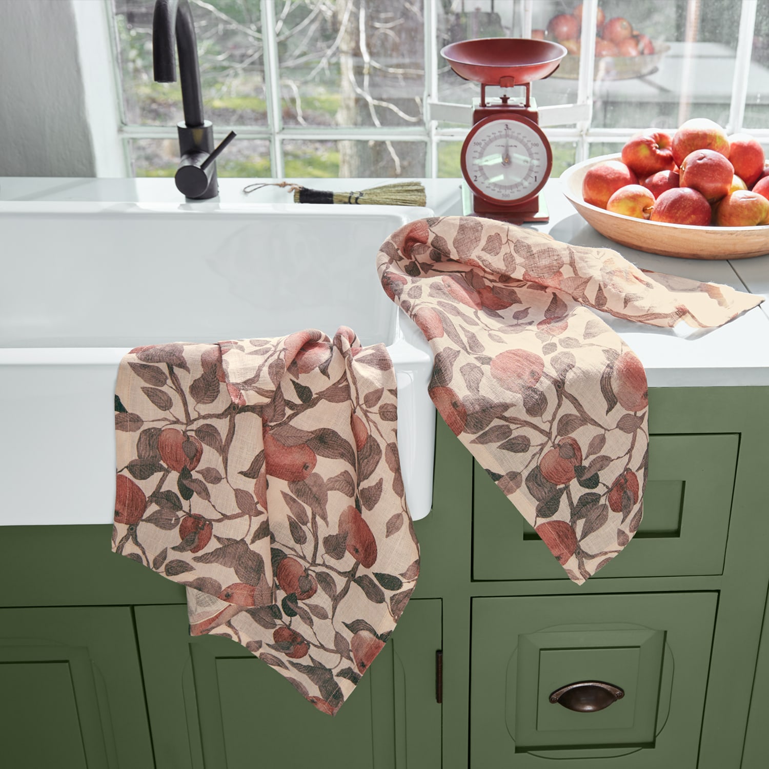 Strofinacci in lino con motivo mele rosse su mobile verde in cucina luminosa