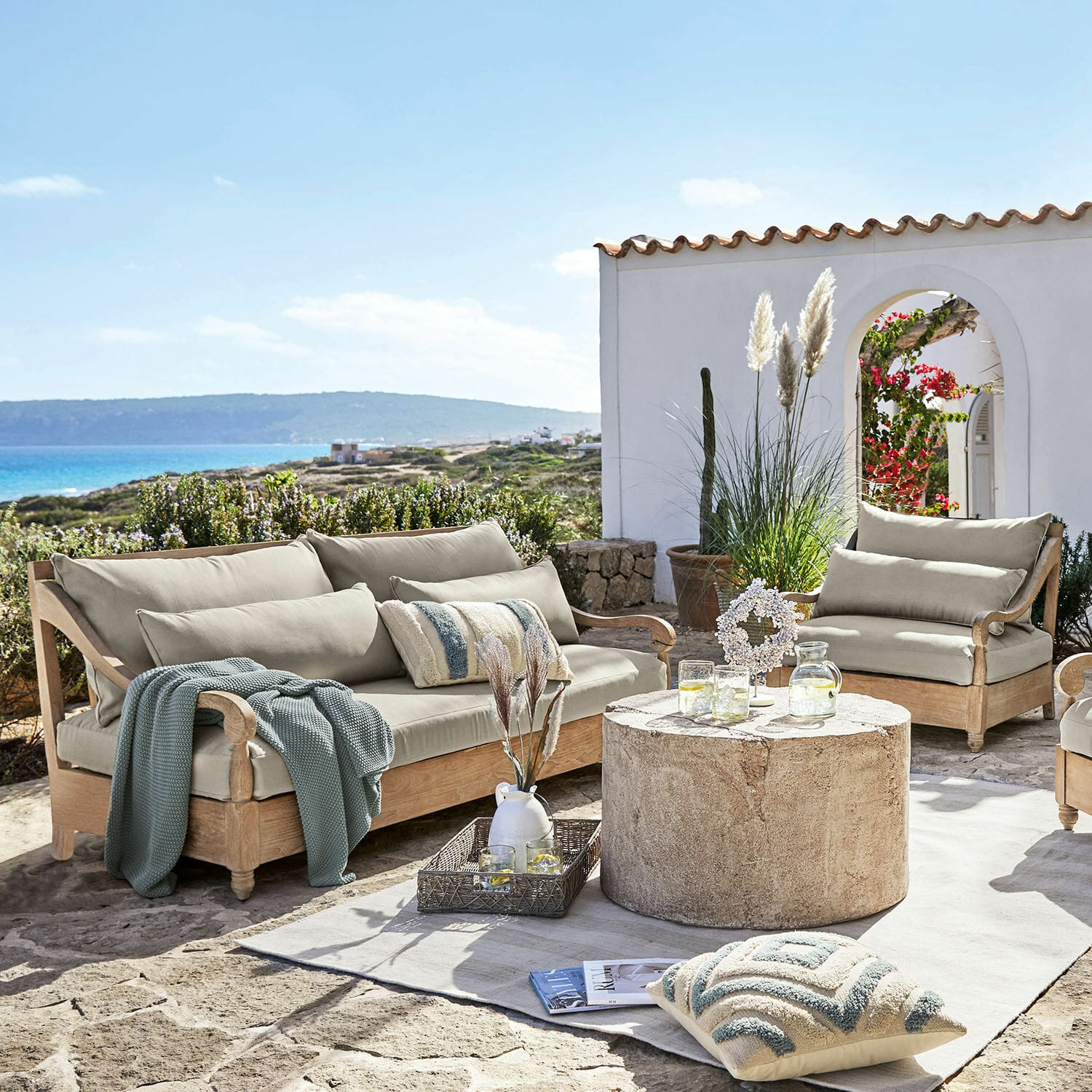 Salottino Montcassin Set di mobili da giardino in legno chiaro con cuscini beige su terrazza in pietra con vista mare