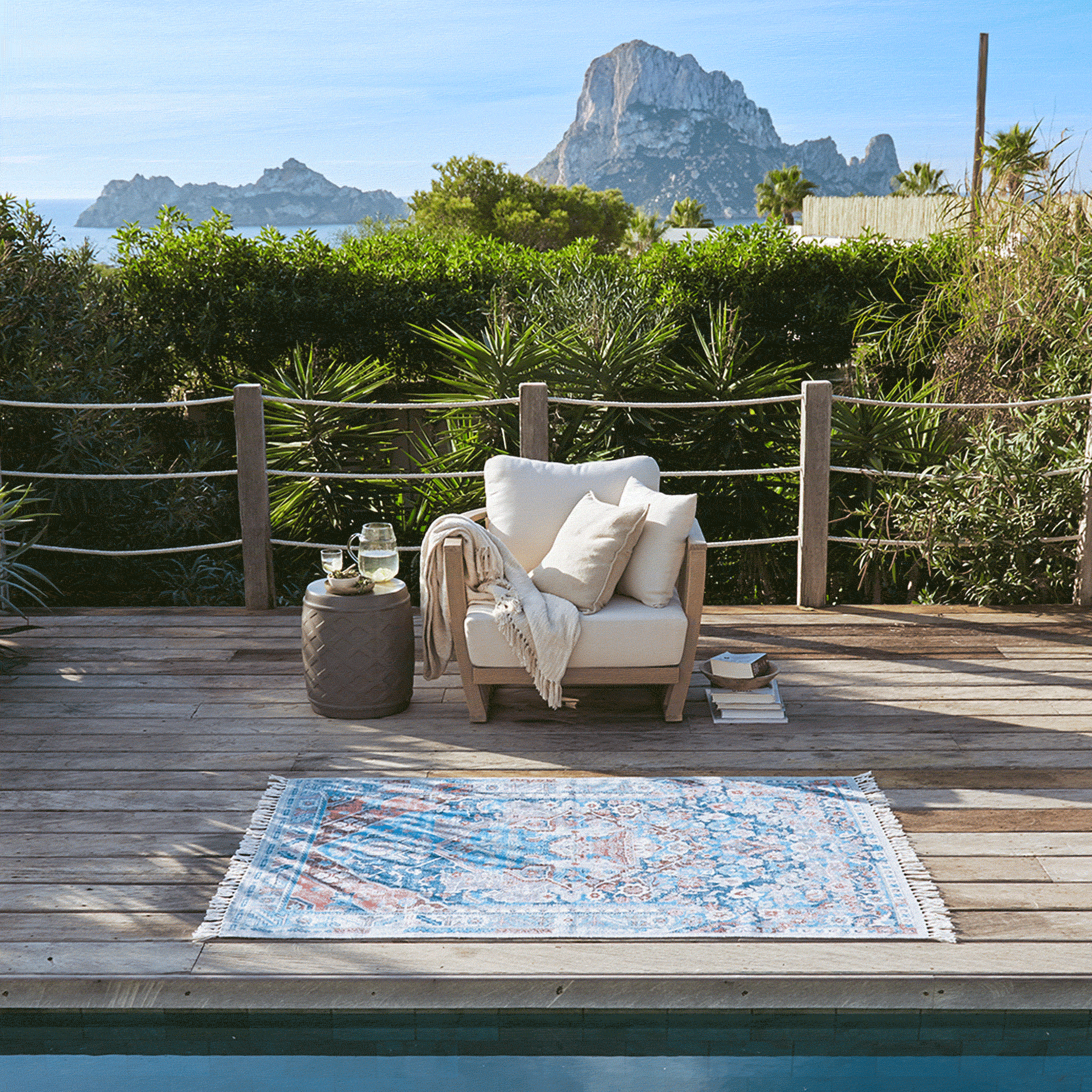 Terrazza in legno con poltrona bianca e tappeto colorato vicino alla piscina con vista sulle montagne