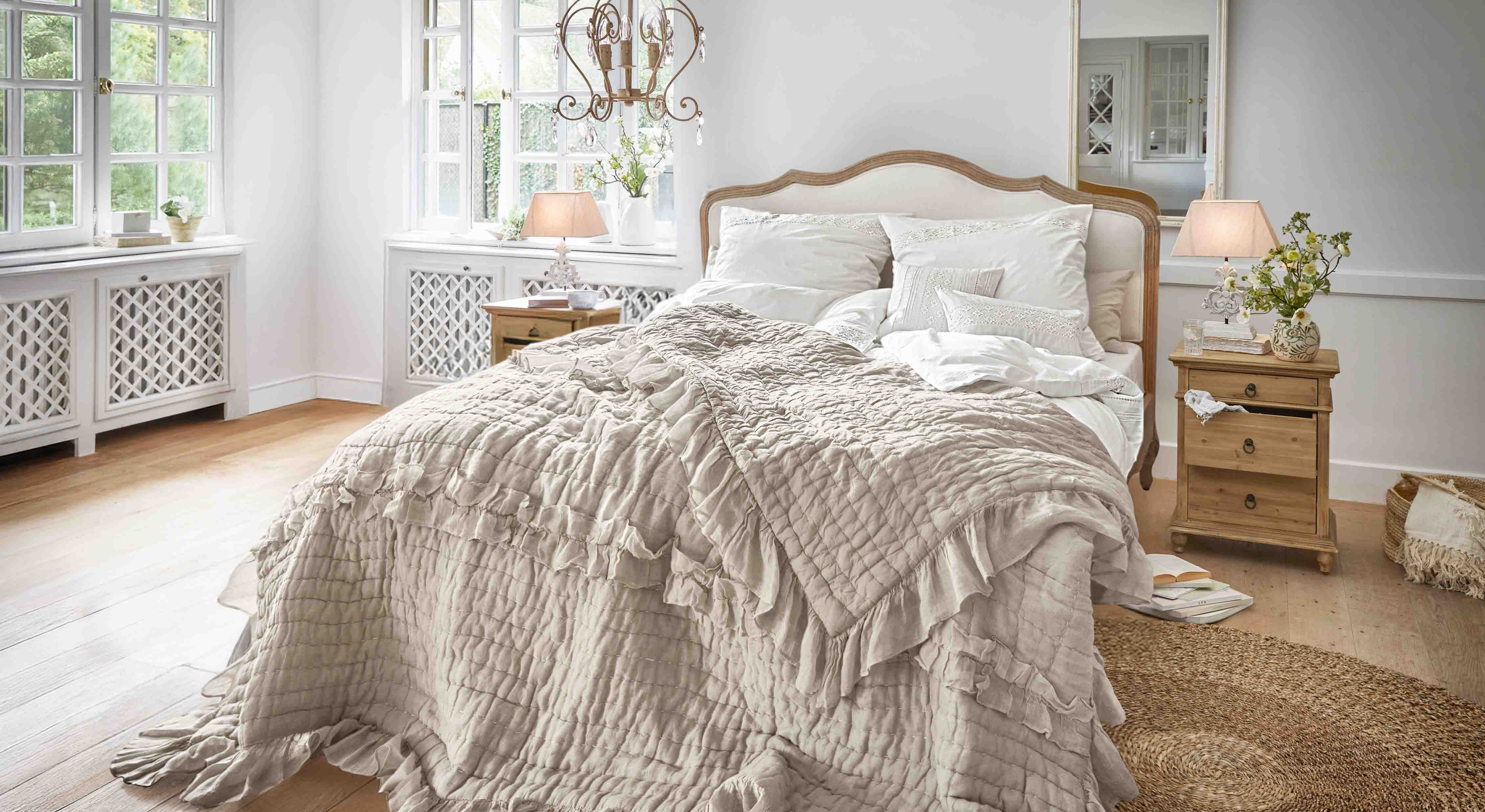 Camera da letto accogliente con letto coperto da trapunta beige con volant e comodini in legno chiaro
