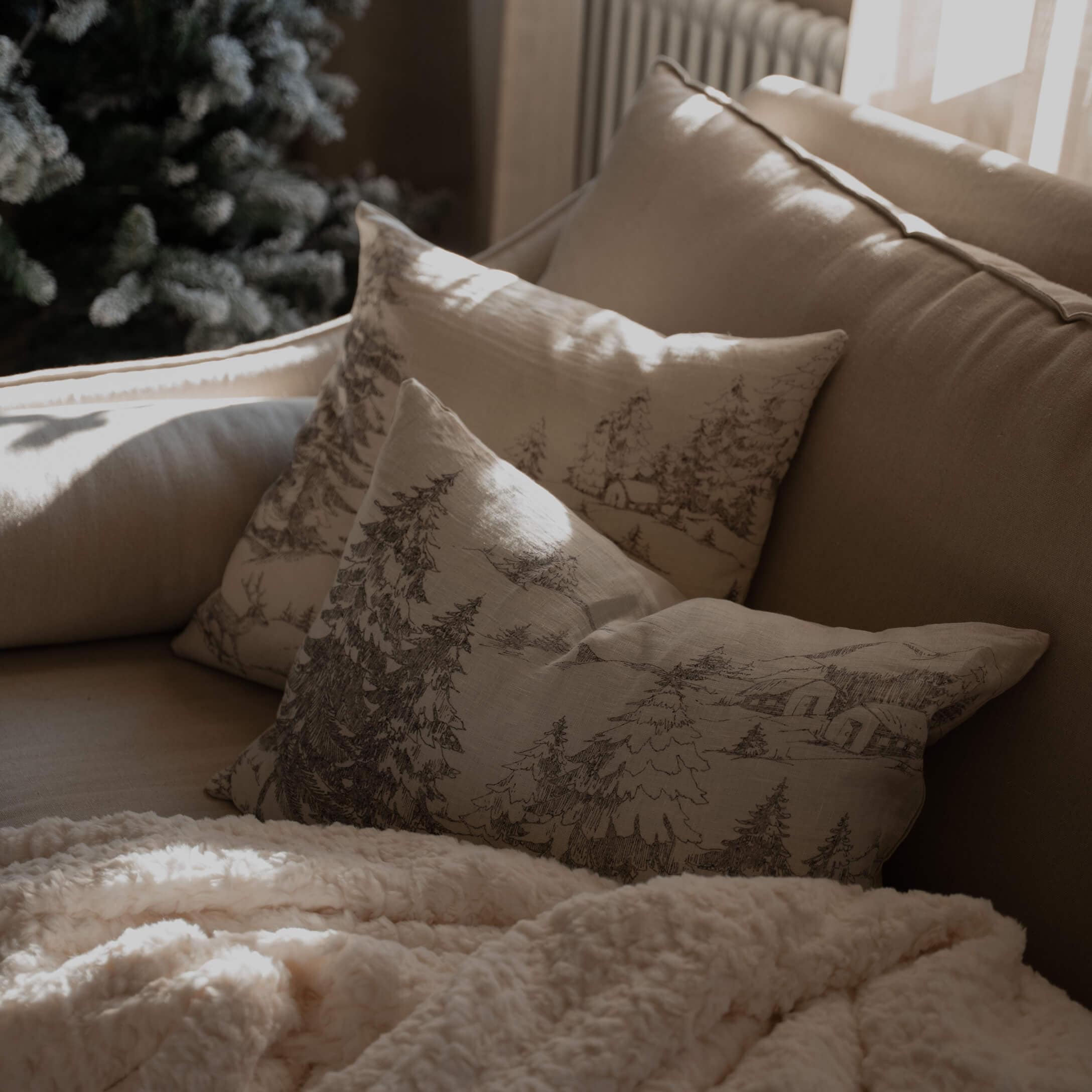 Divano beige con cuscini stampati con motivo bosco e coperta morbida color crema per soggiorno accogliente