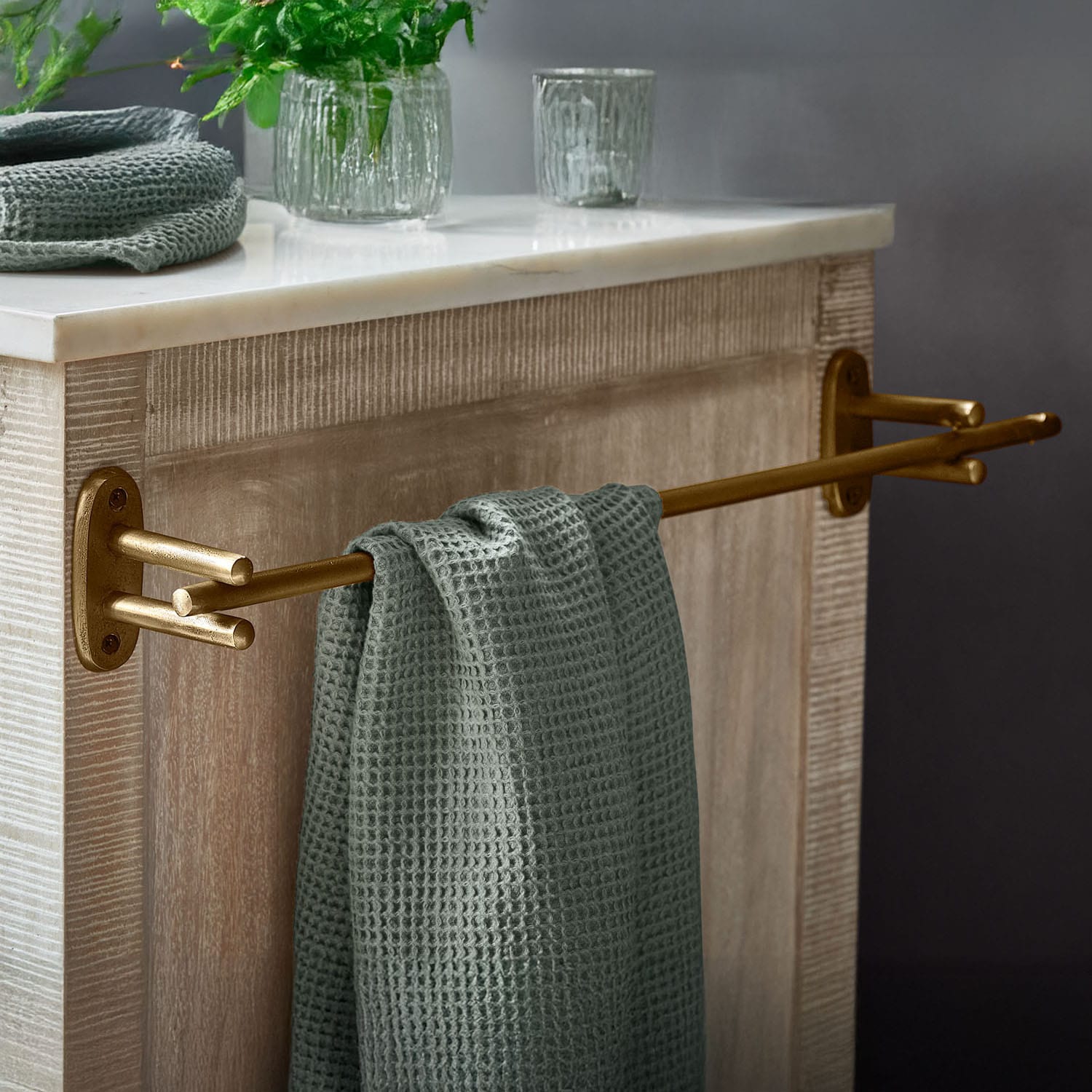 Porta asciugamani in metallo dorato con asciugamano verde a nido d'ape su mobile in legno con piano in marmo