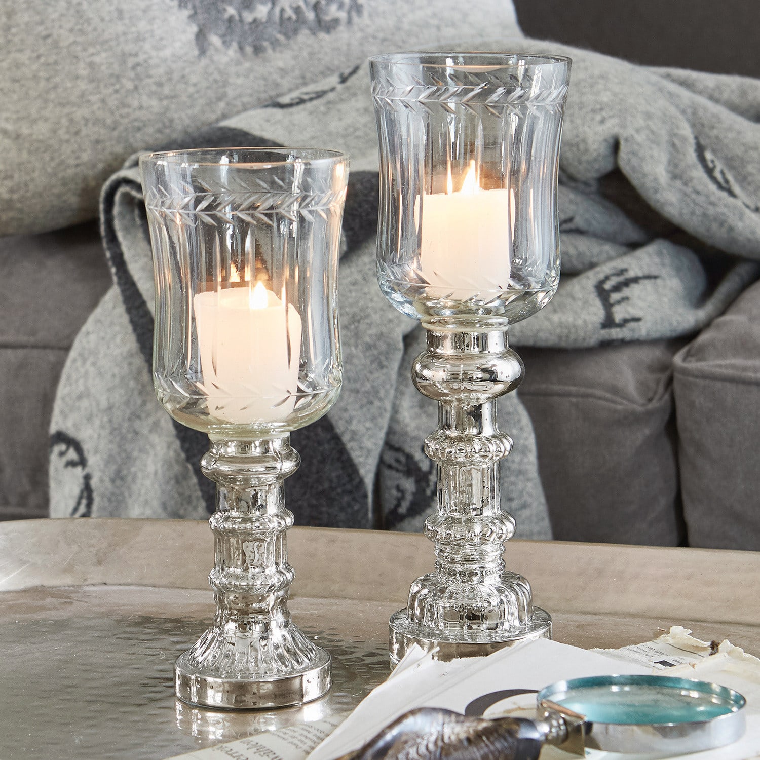 Due portacandele in vetro con candele bianche su tavolo argentato, decorazione elegante per interni