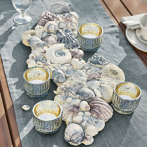Runner decorativo con conchiglie grigie e quattro portacandele in vetro dorato su tavolo in legno