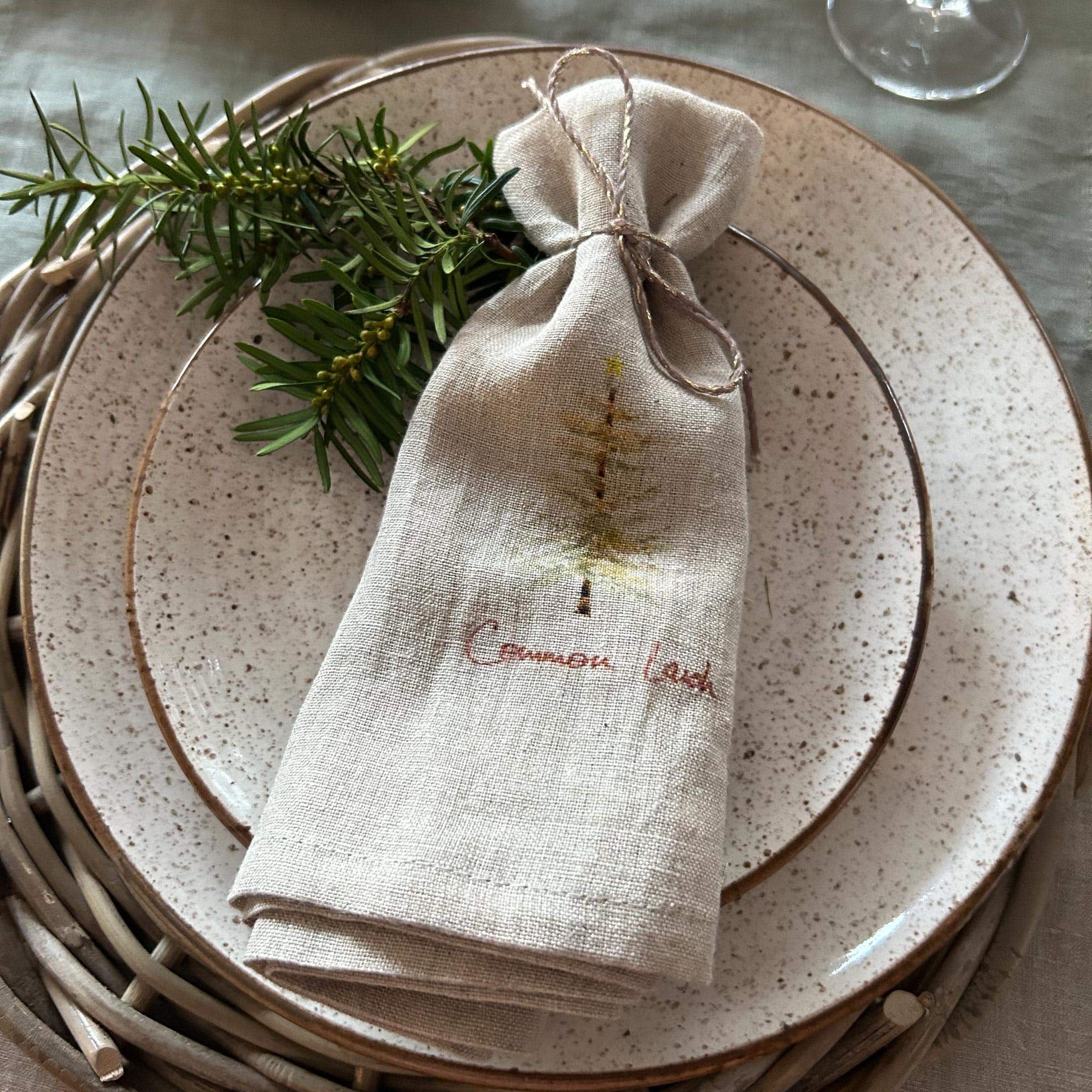 Sacchetto di lino beige con stampa albero su piatto in ceramica con rami verdi