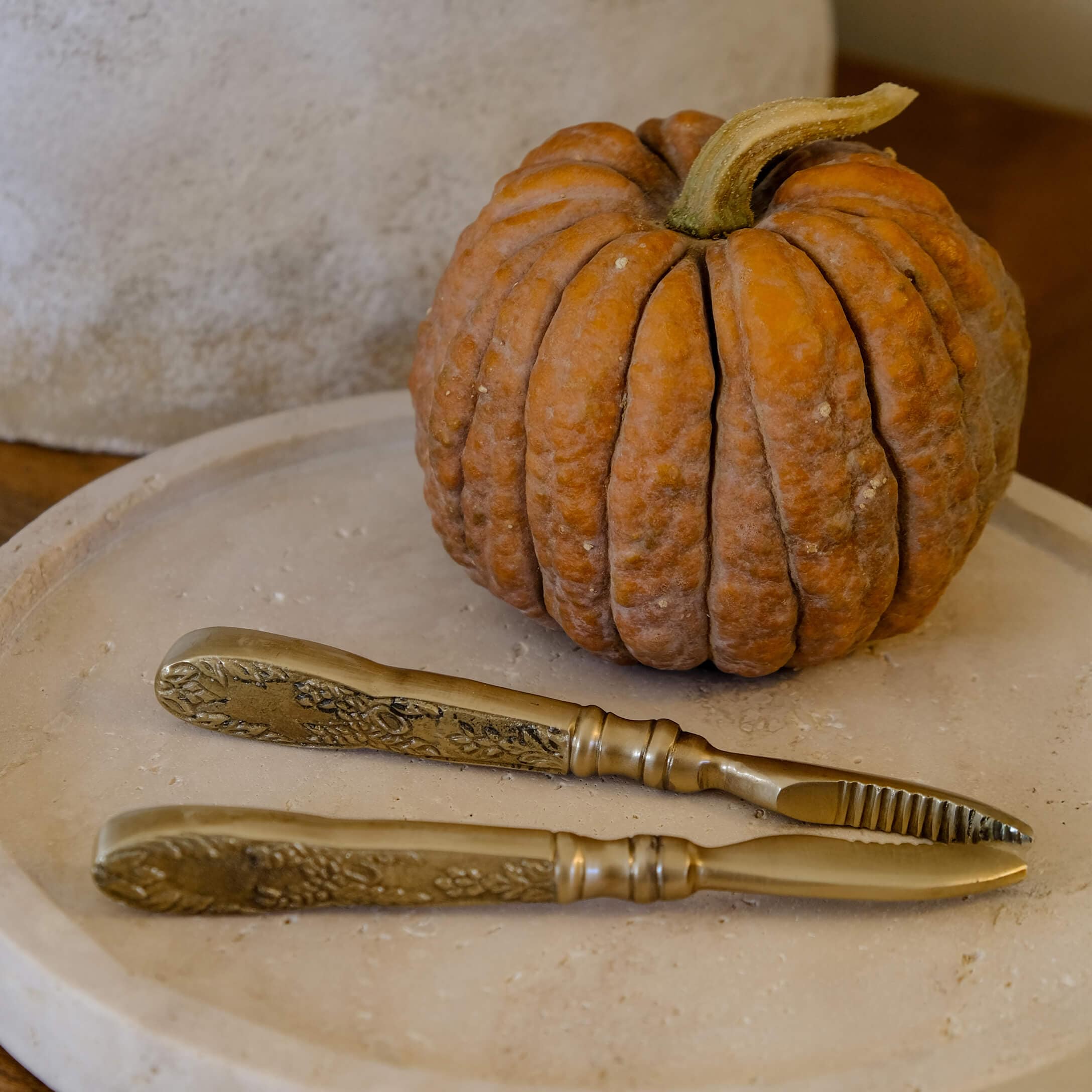 Set di coltelli in ottone con manici decorati su vassoio beige accanto a zucca arancione