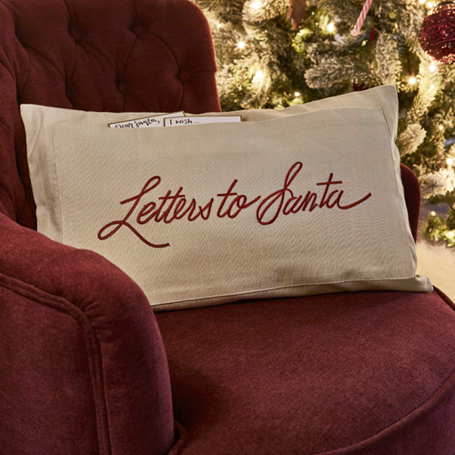 Federa beige con scritta Letters to Santa su poltrona bordeaux vicino all'albero di Natale