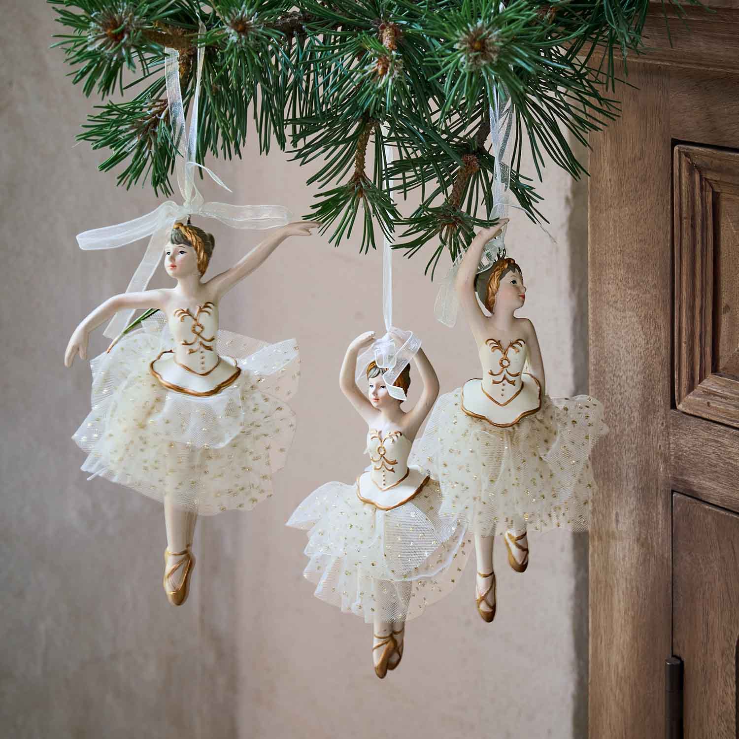 Tre ballerine bianche con gonne di tulle e dettagli dorati appese a un ramo di abete