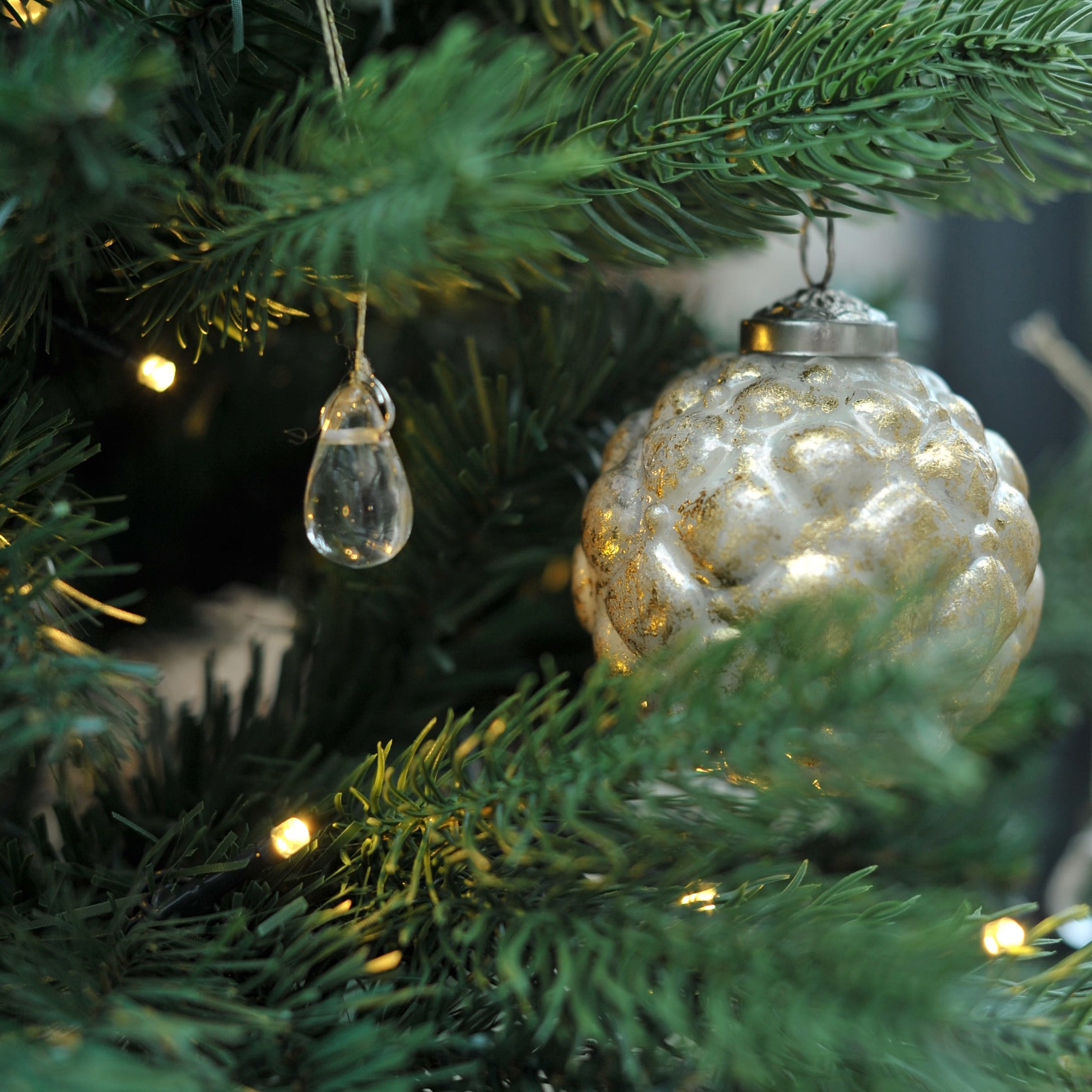 Pallina di Natale dorata in vetro e decorazione trasparente su albero verde con luci natalizie