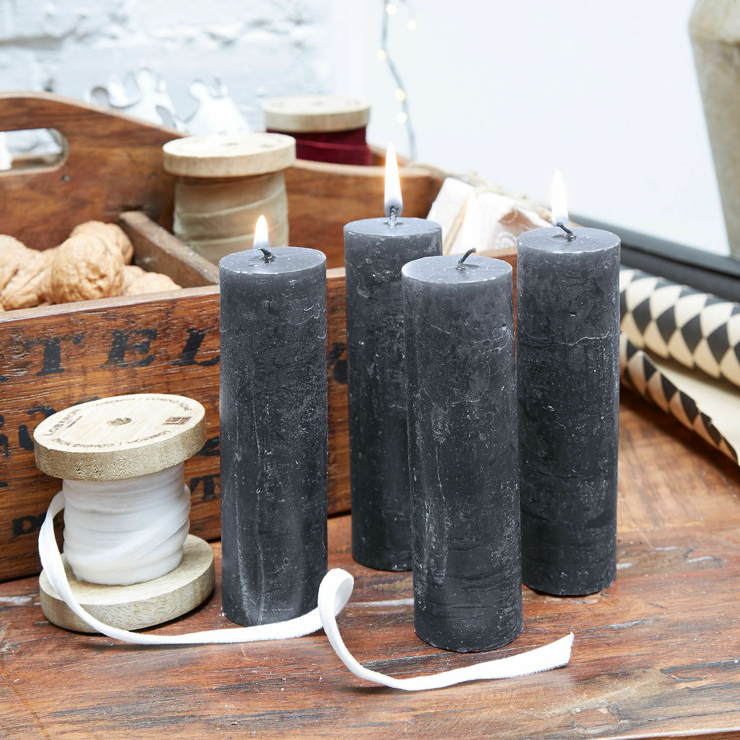 Set di 4 candele Muriel Quattro candele nere in cera naturale su tavolo di legno con rocchetti decorativi e noci