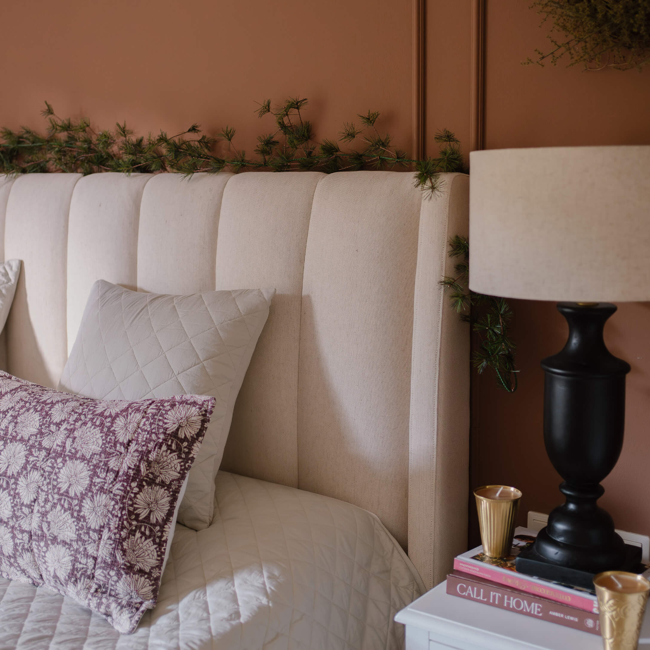 Testata del letto imbottita beige con cuscini e lampada su comodino in camera accogliente