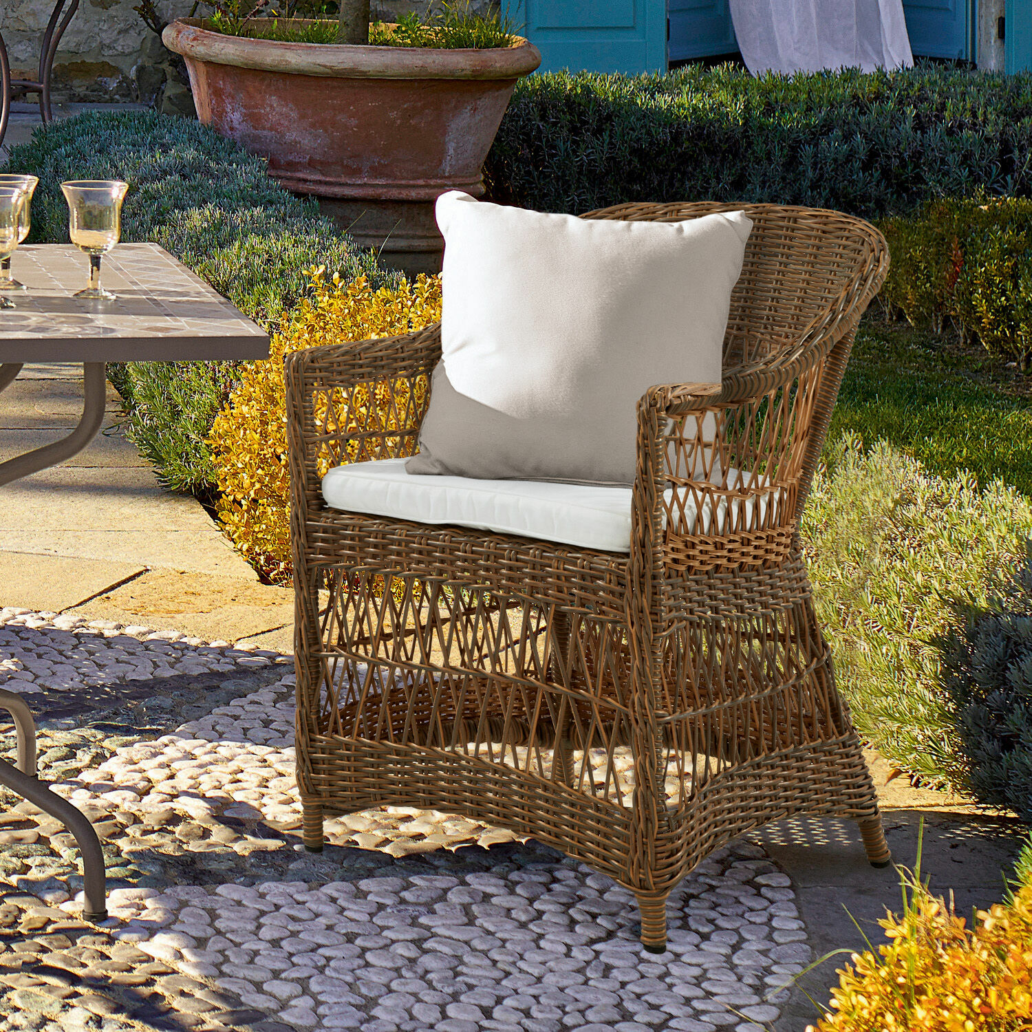 Poltrona Garden Grove Poltrona in rattan con cuscino bianco su pavimento in pietra in giardino all'aperto