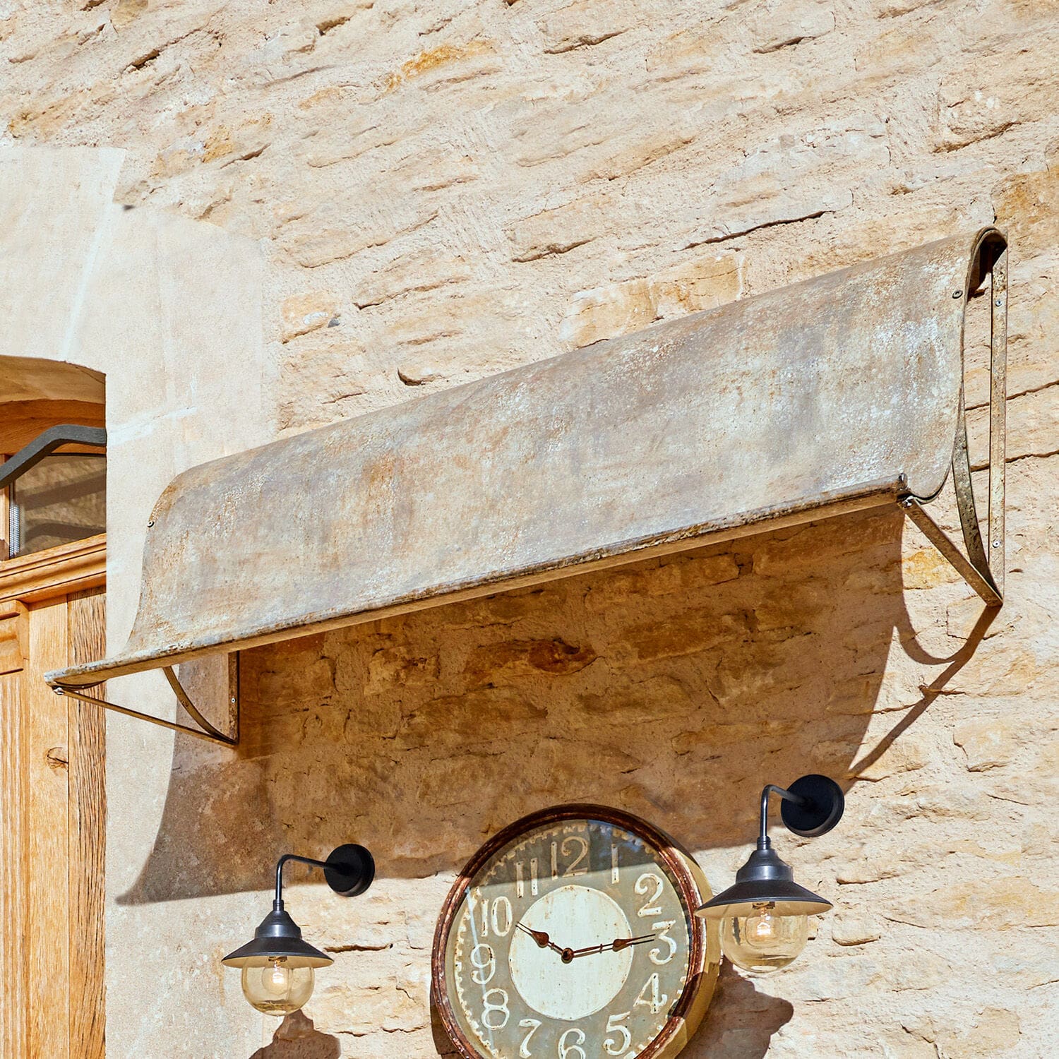 Tettoia Lison Tettoia in metallo grigio invecchiato su muro di pietra con orologio e lampade nere