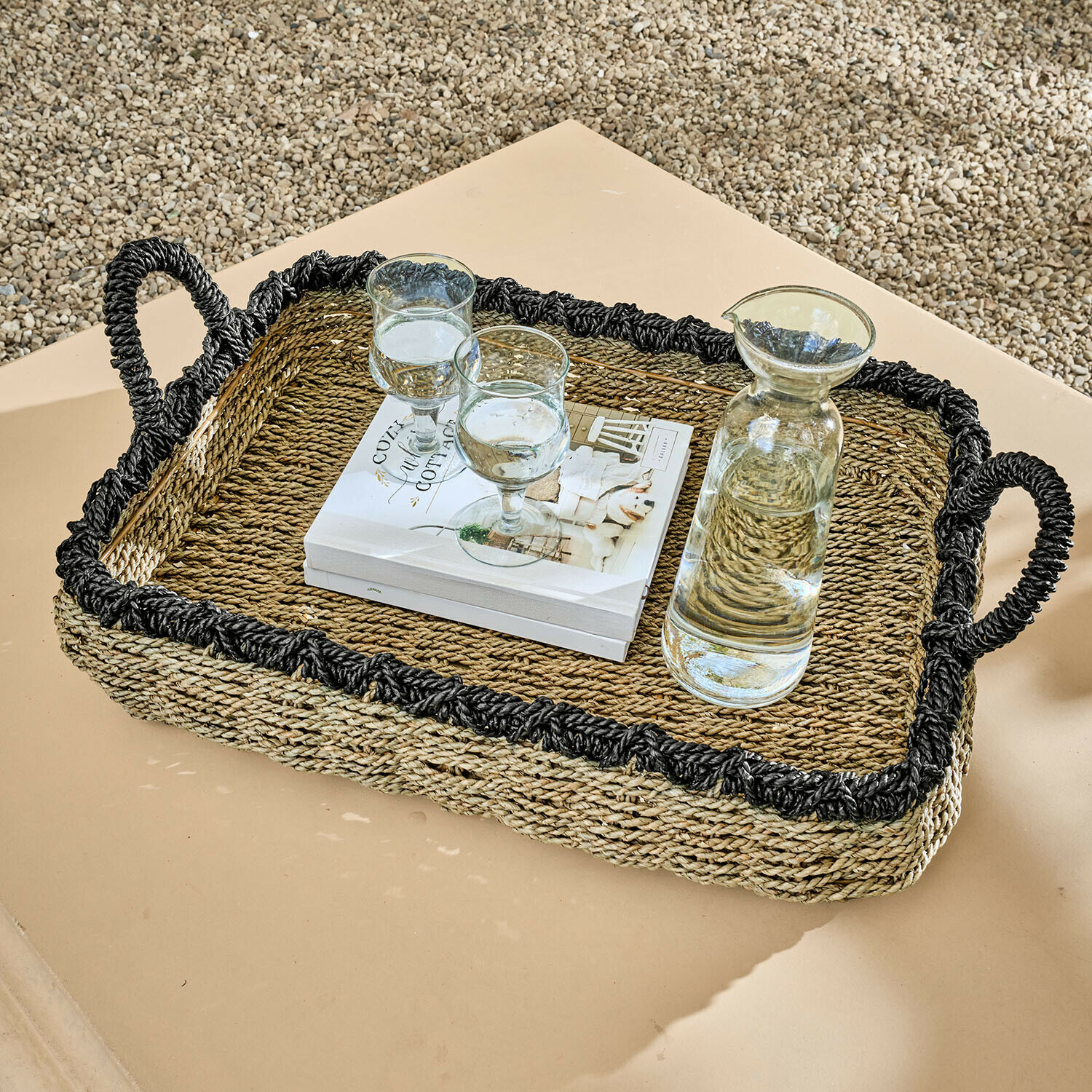 Vassoio Tarevo Vassoio rettangolare in erba marina intrecciata con bordo nero e manici, con caraffa e bicchieri su tavolo