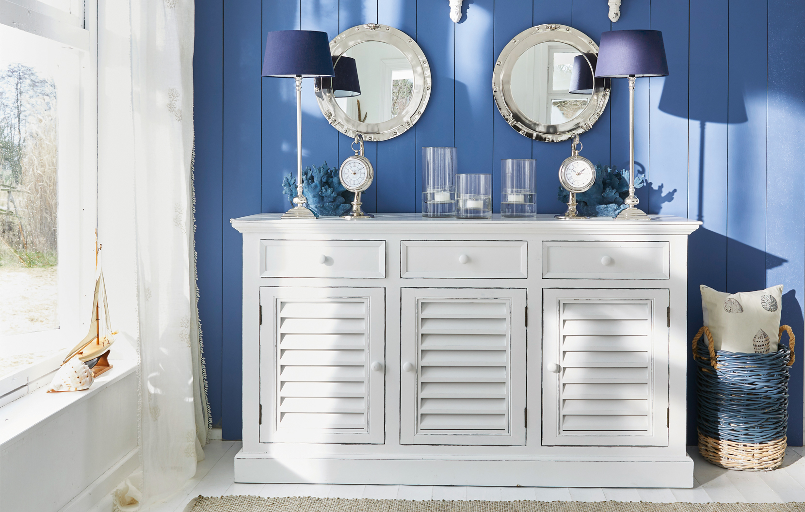 Credenza bianca in legno con ante a persiana su parete blu con decorazioni marine