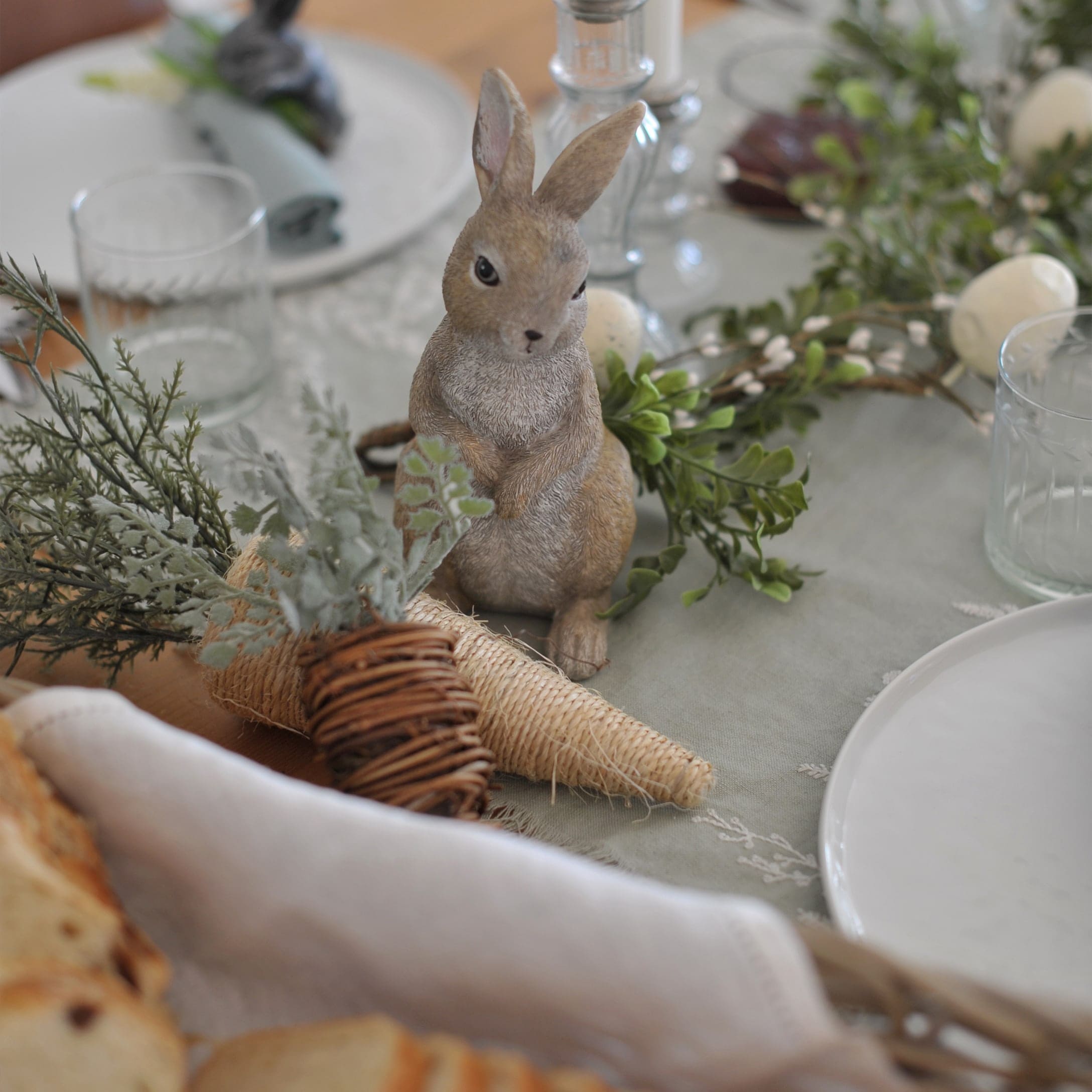 Coniglio decorativo su tavola con ornamenti naturali e bicchiere, decorazione primaverile