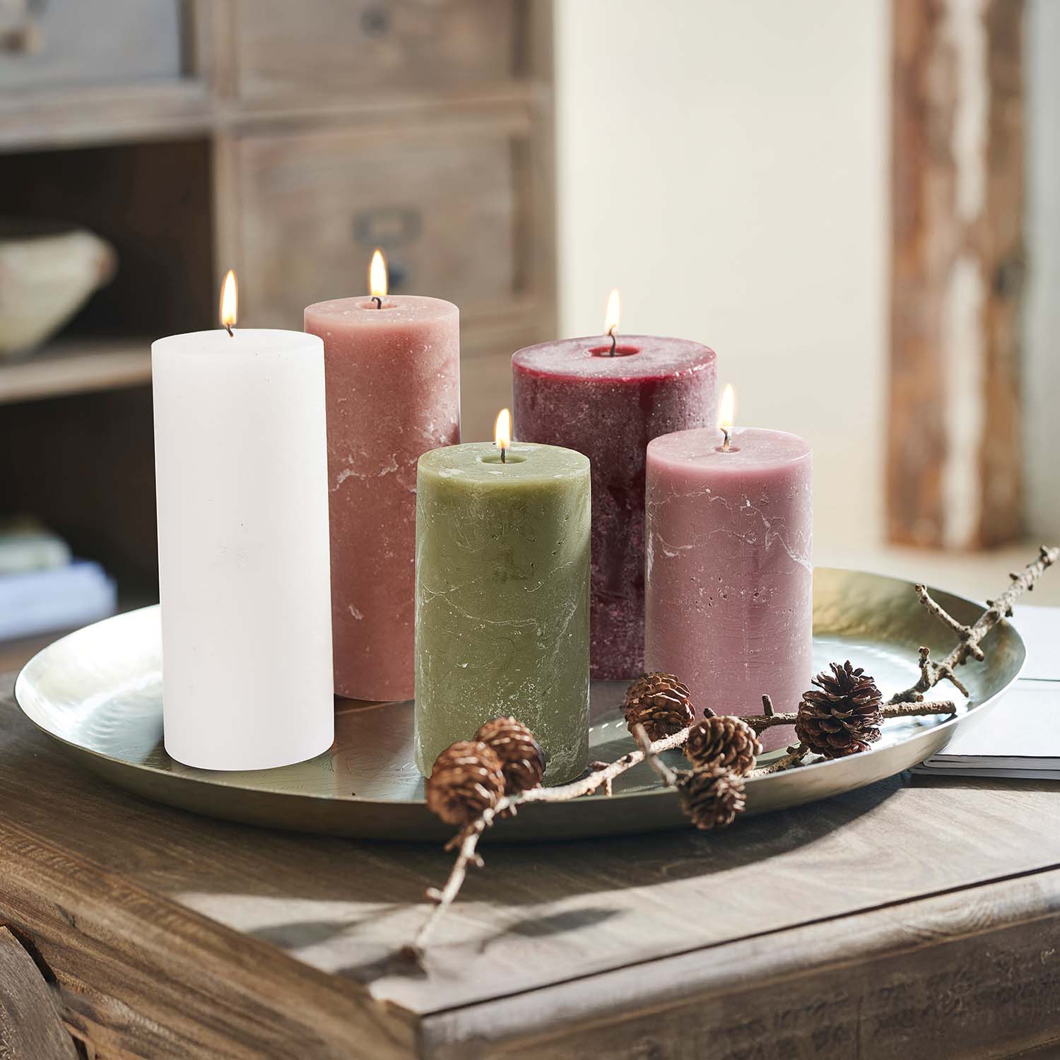 Set di cinque candele colorate su un vassoio in metallo con pigne decorative su tavolo in legno