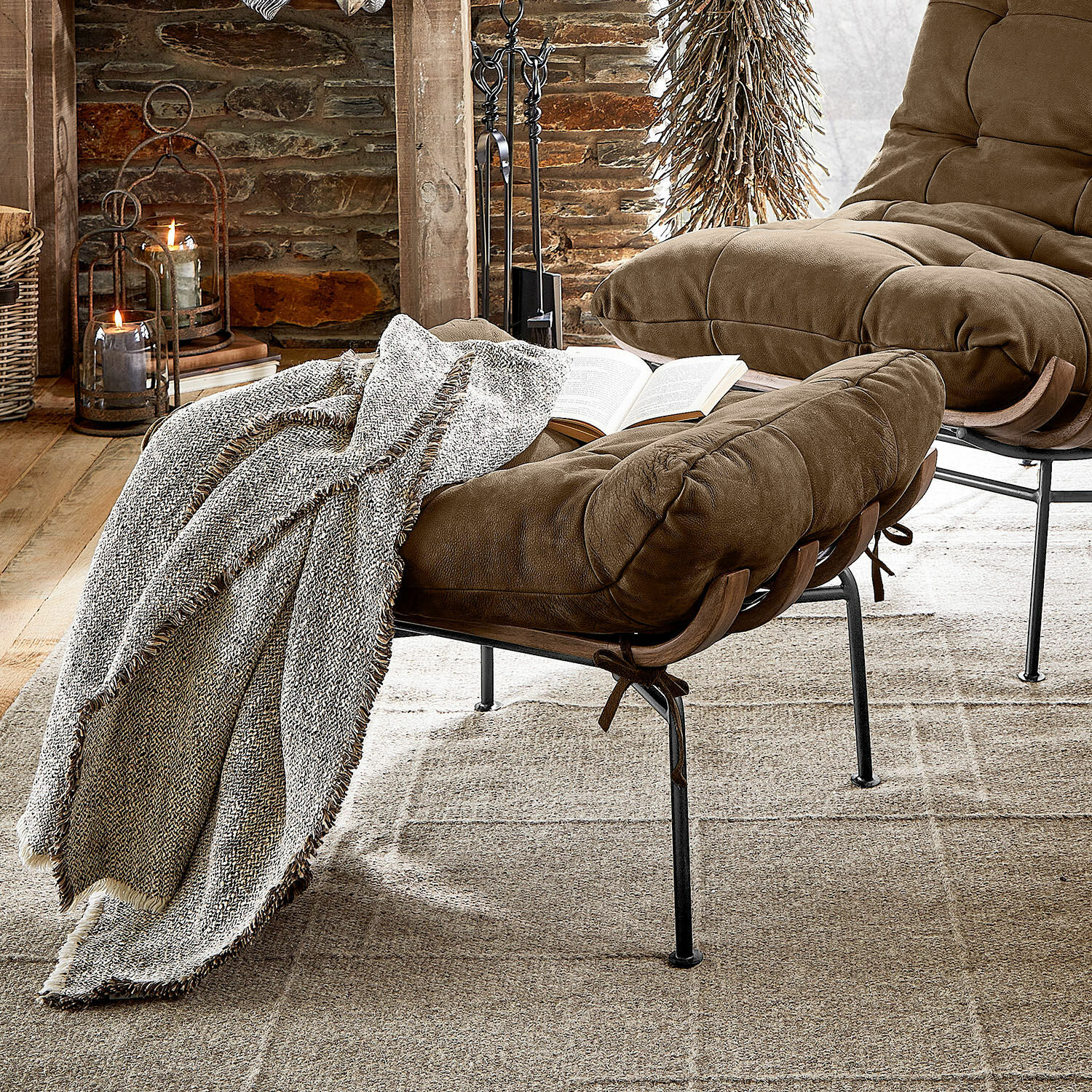 Poggiapiedi Horraine Poltrona marrone in tessuto morbido con poggiapiedi e coperta grigia su tappeto beige in ambiente rustico